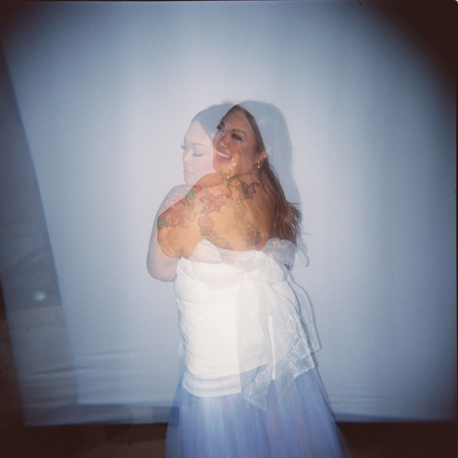 Woman in white strapless top and blue skirt with floral tattoos, smiling in a dreamy double-exposure photo.