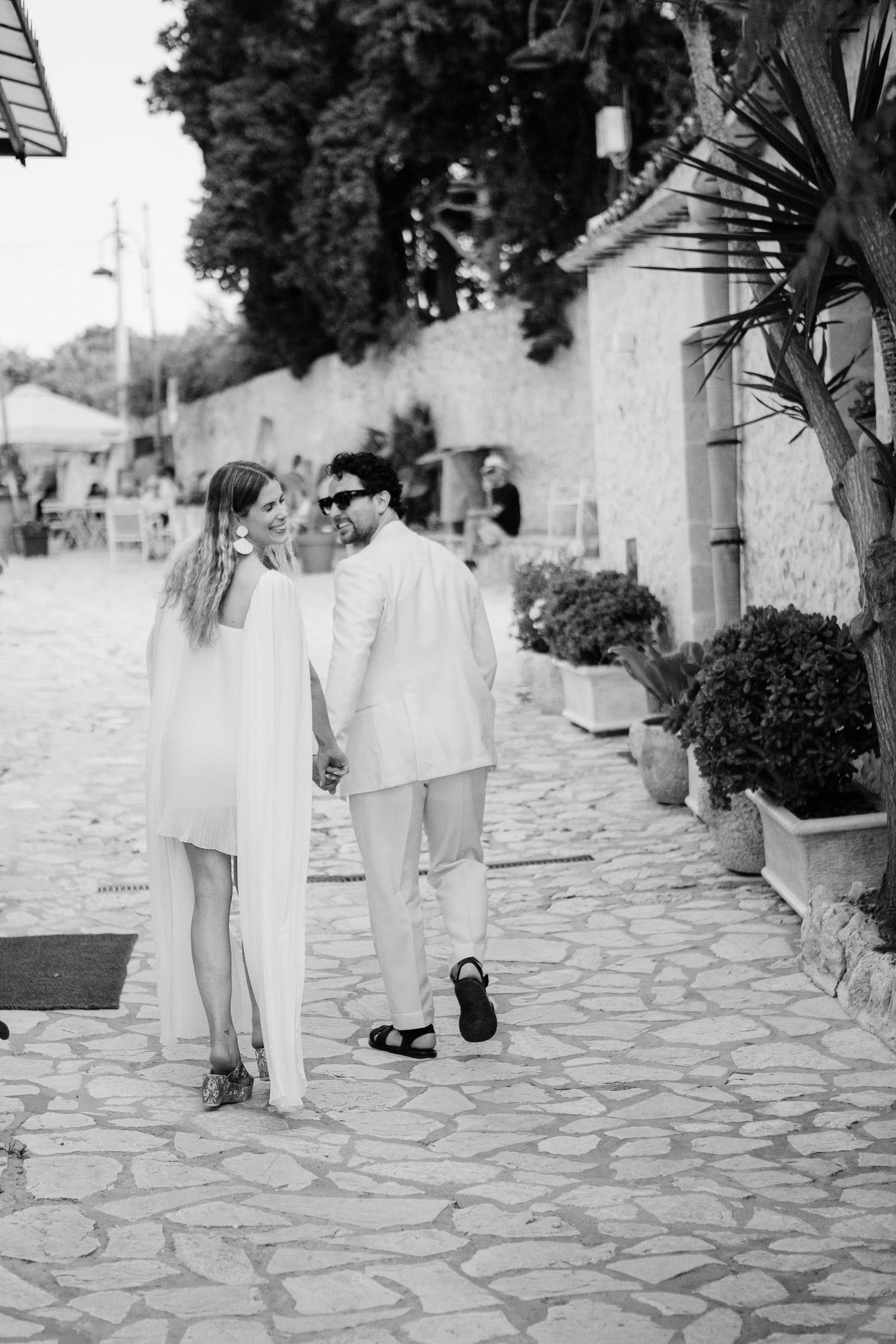 A sequence of black and white photos showing people walking on a stone paved path in white clothing.
