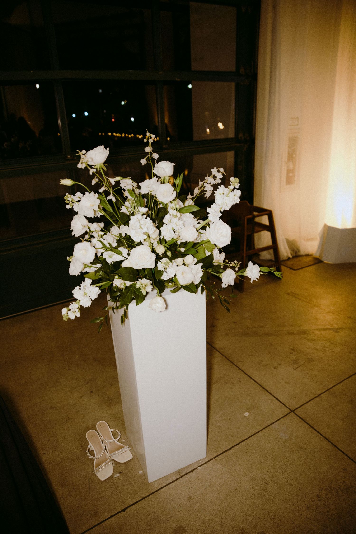 A white floral arrangement in a modern square vase shown from multiple angles on a concrete floor.