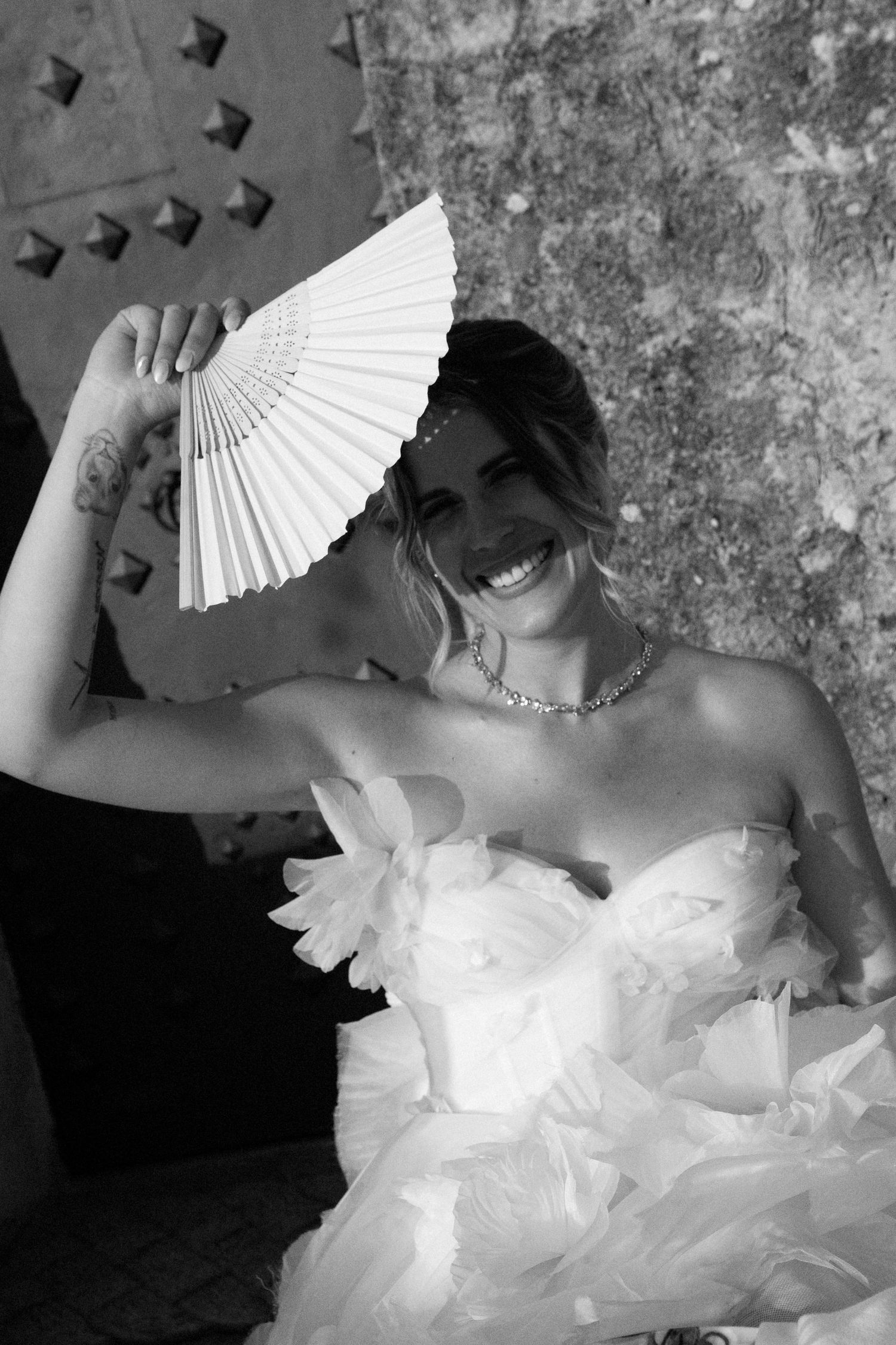 A series of artistic black and white photographs showing a white paper fan and flowing wedding dress details.