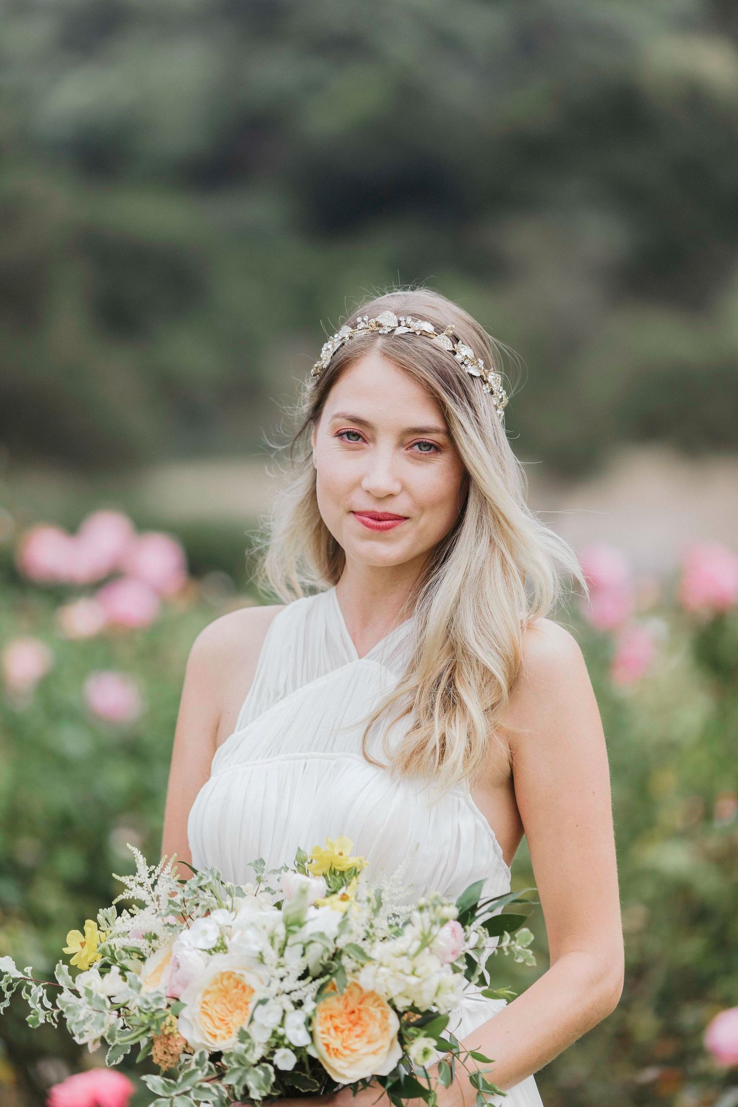 A bouquet of peach and white flowers is held in a garden setting with roses blooming in the background.
