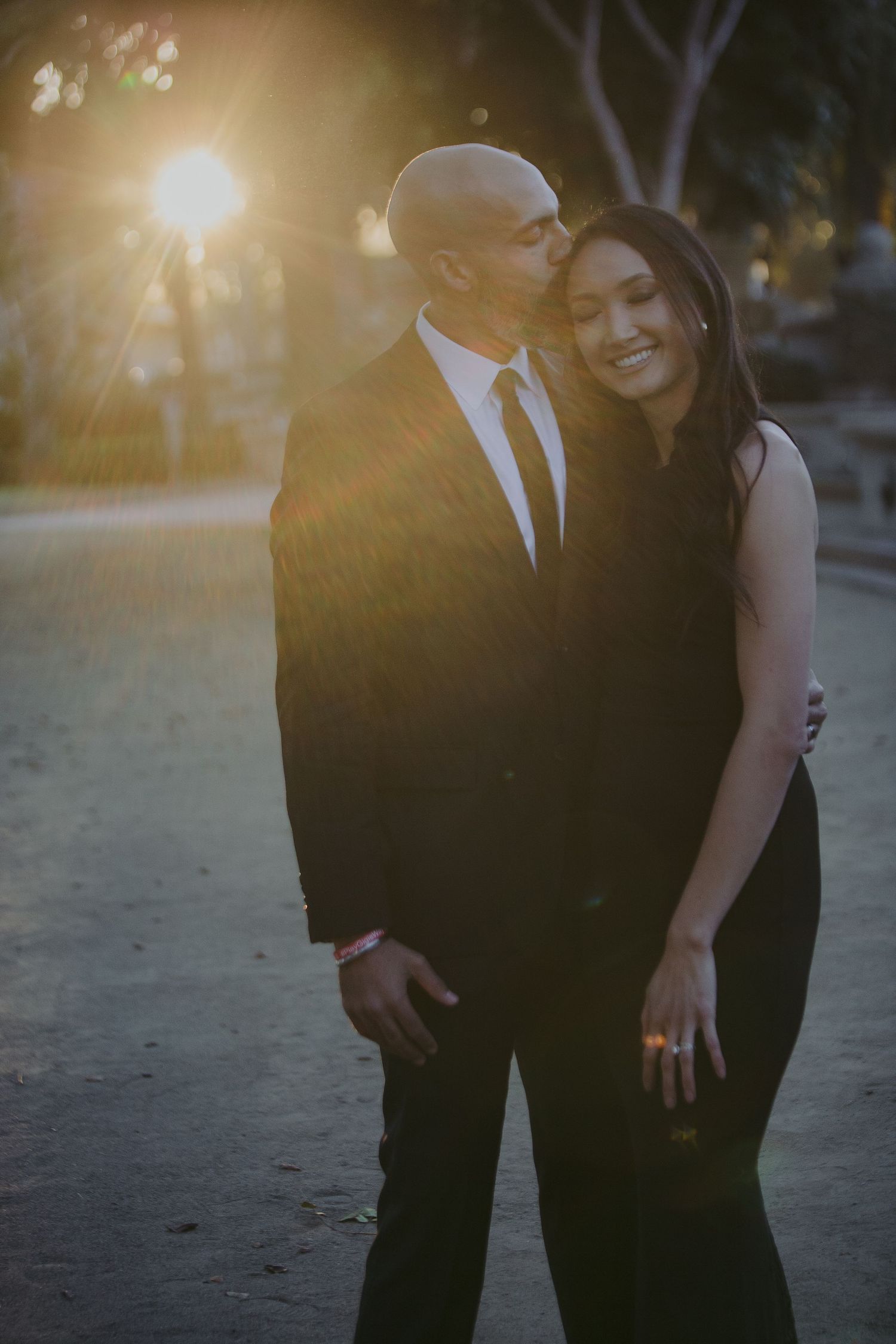 A couple embraces and laughs together at sunset, with golden sunlight creating a warm backlit glow behind them.