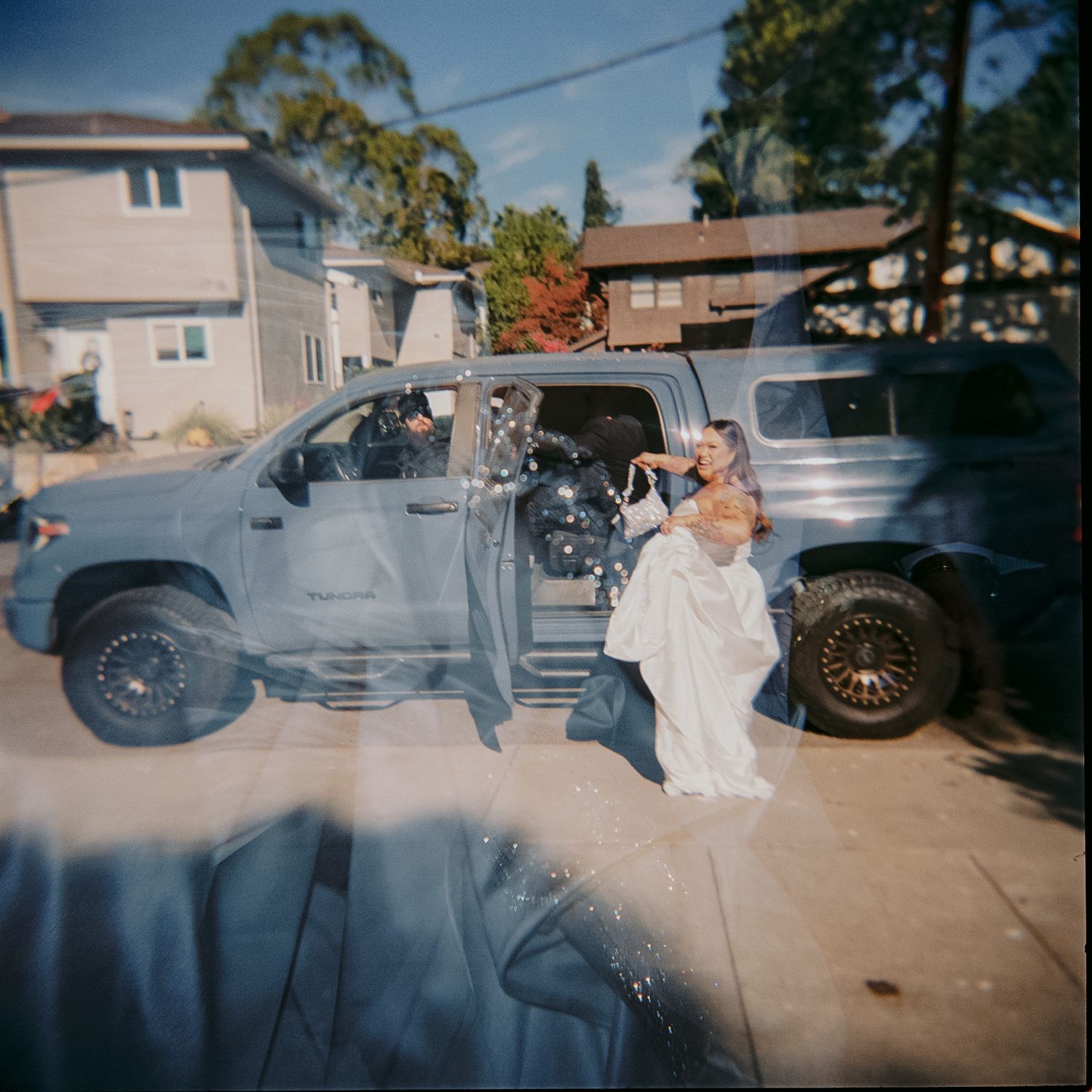 A vintage car creates a dramatic smoke effect during a wedding photo shoot in a suburban driveway.