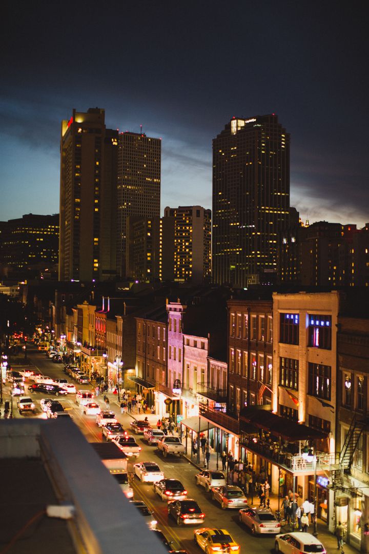 Nighttime cityscape showing illuminated high-rise buildings and storefronts along a bustling commercial street at dusk.