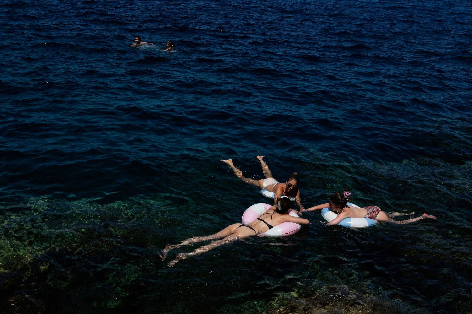 Two people float side by side in dark blue ocean water while wearing swimsuits and snorkel gear.