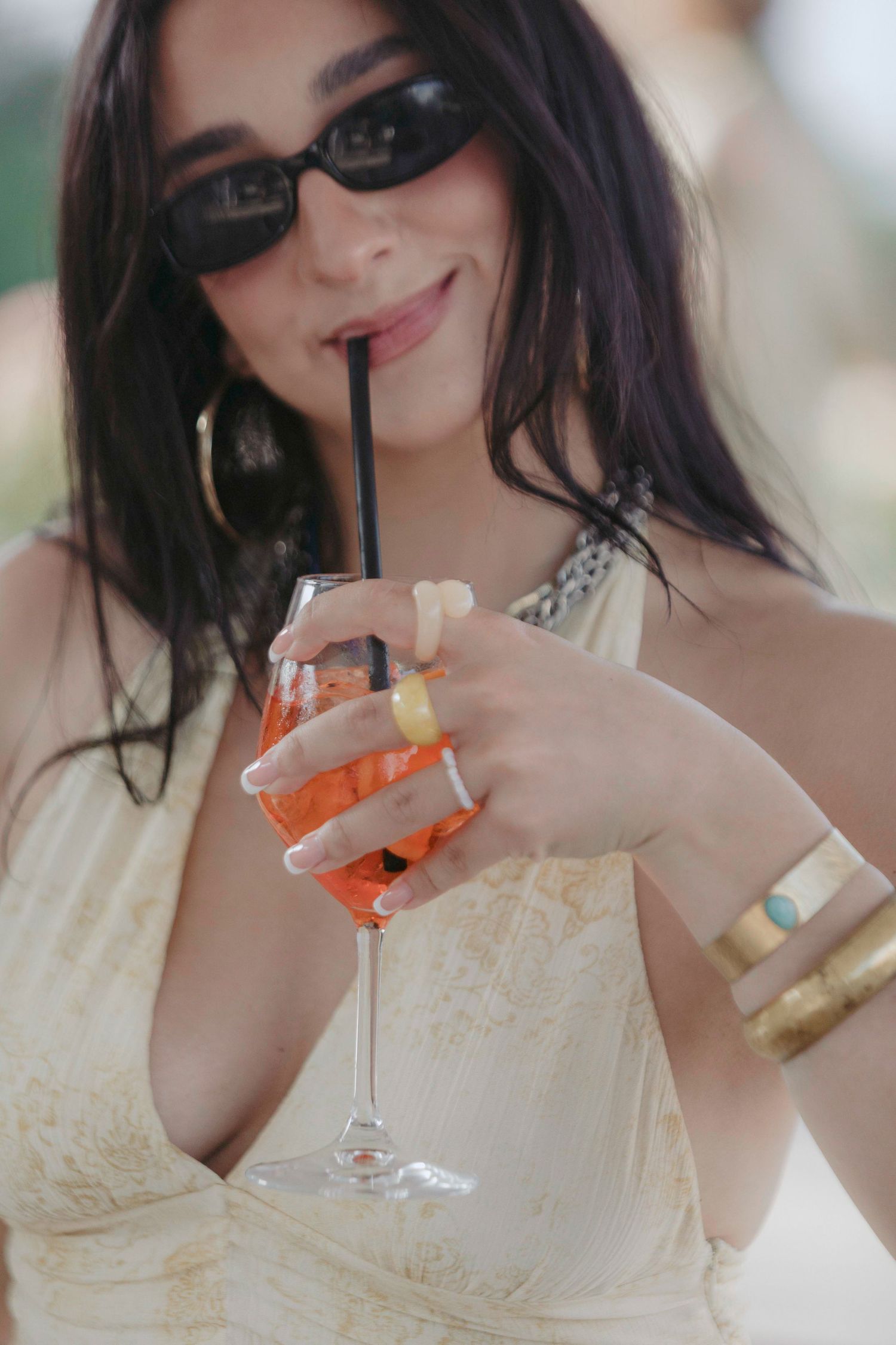 Woman in white dress sips cocktail through straw while wearing sunglasses in series of progressive shots.