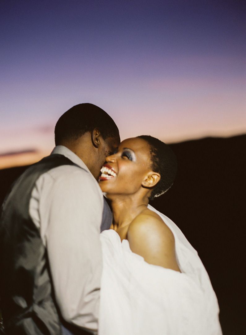 A couple shares an intimate moment during sunset in their wedding attire with a soft purple sky backdrop.