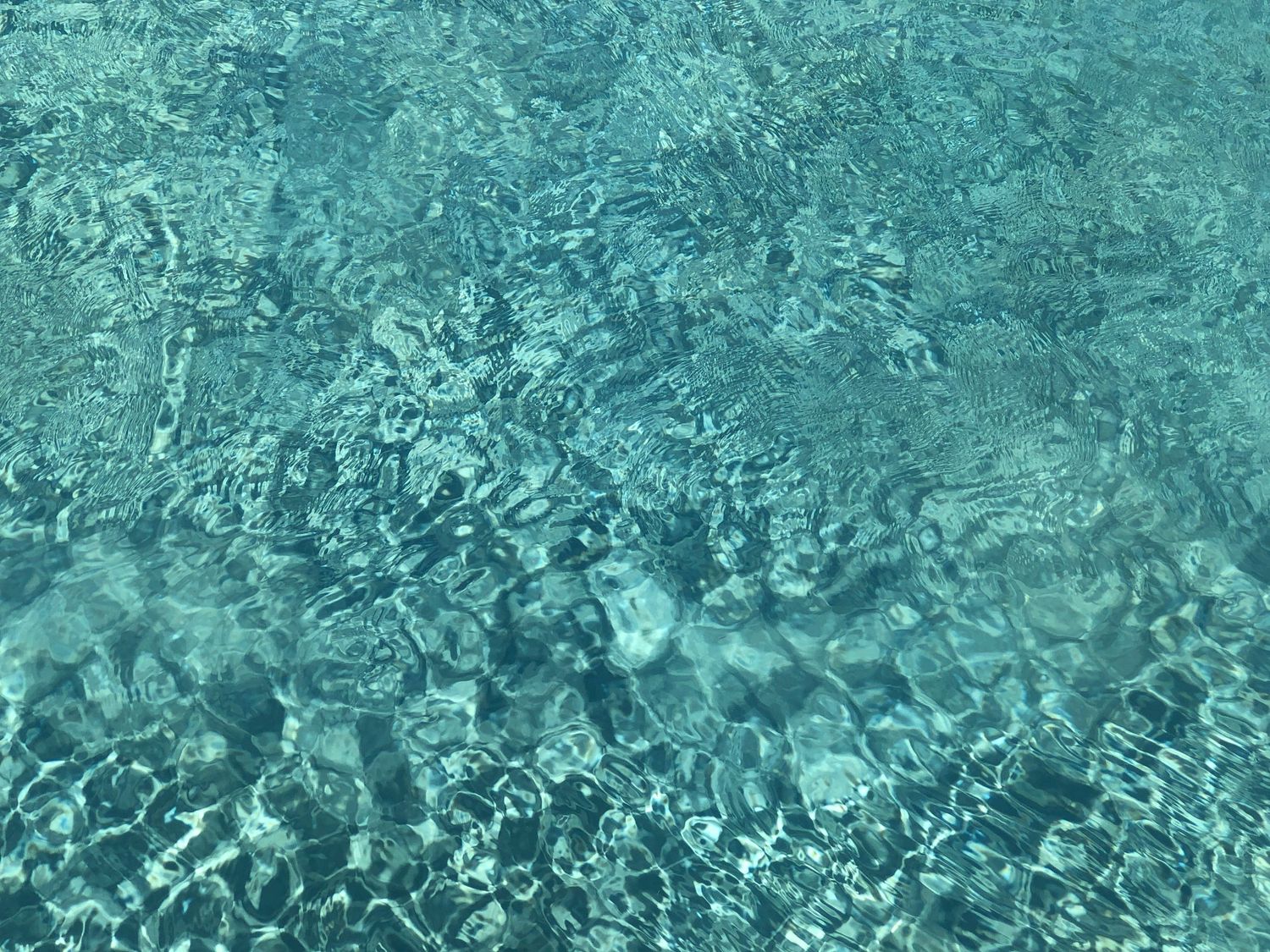 Clear turquoise water ripples in a swimming pool creating mesmerizing patterns and reflections in sunlight.