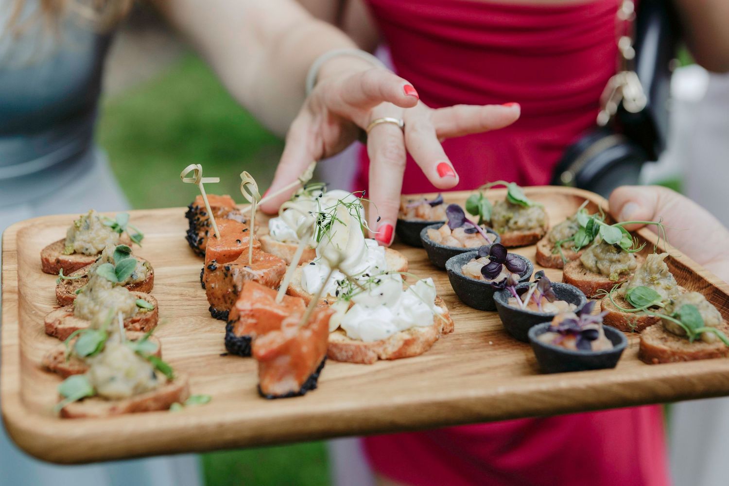 A wooden serving board displays an assortment of seafood appetizers and canapes with garnishes.