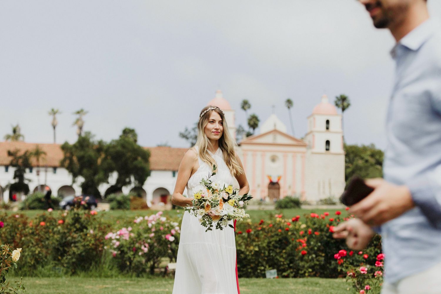 A couple celebrates their wedding day in a beautiful garden setting with white flowers and palm trees in the background.