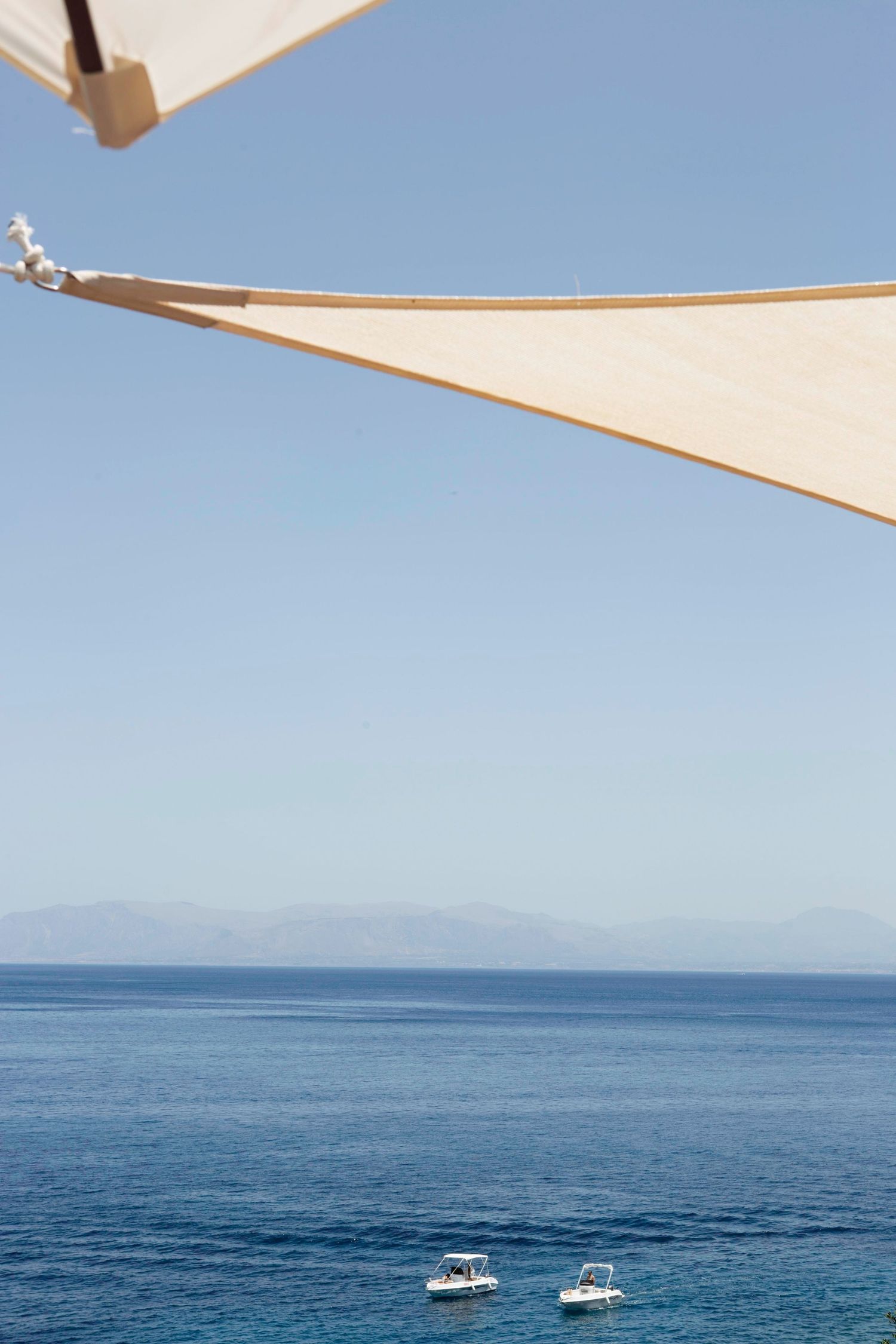 Two small white boats float on calm blue ocean waters with distant mountains visible on the horizon.