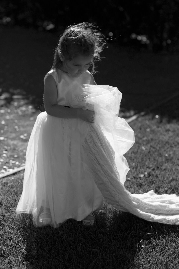 A young child in a flowing white dress twirls on grass in black and white photography.