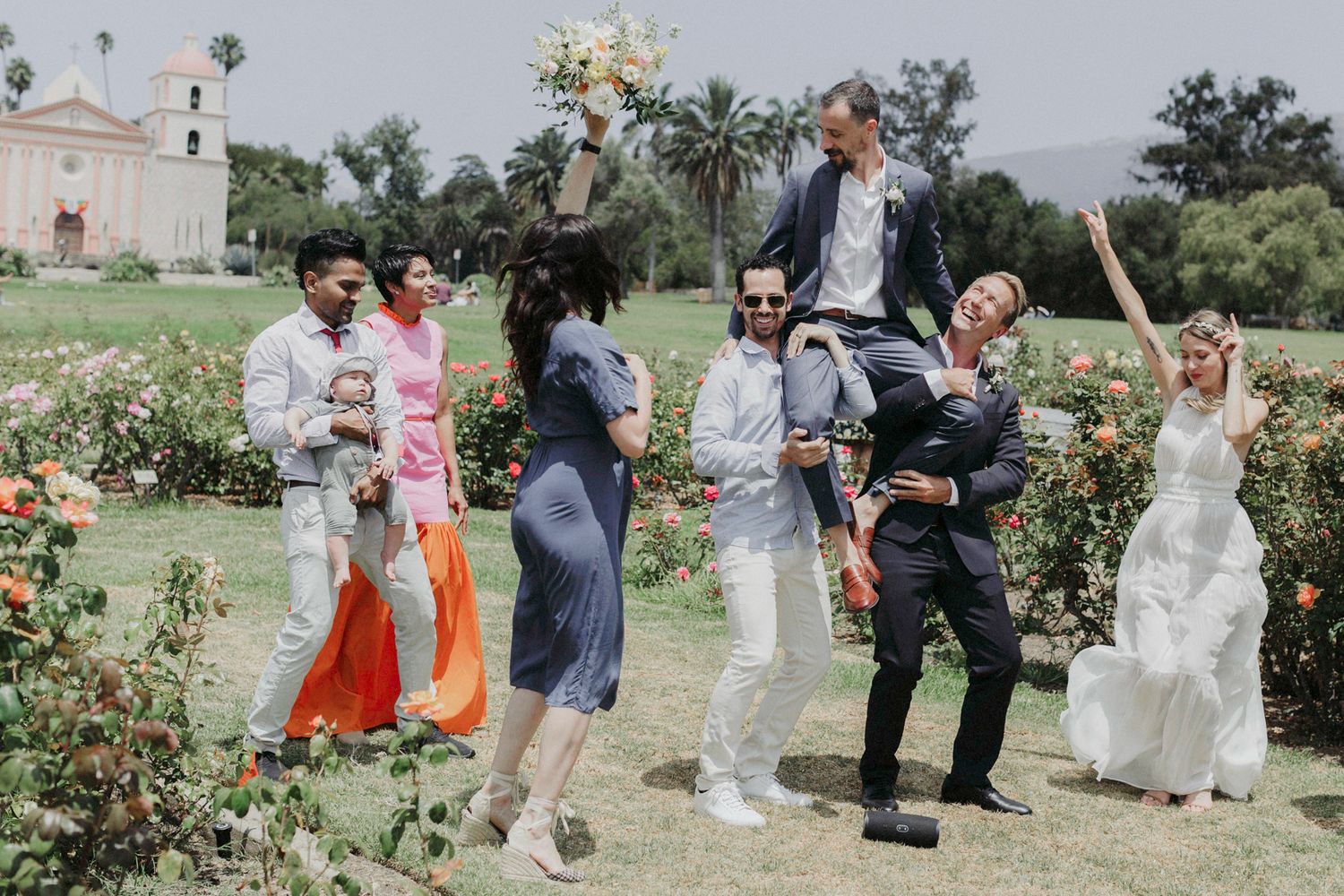 Wedding party poses in a scenic garden setting with colorful flowers and lush greenery in the background.