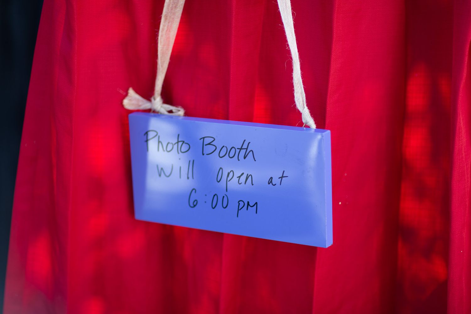 A blue sign hanging on a red curtain announces 'Photo Booth will open at 6:00 pm'.