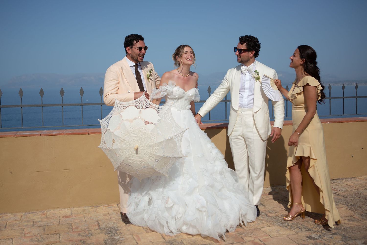 A wedding party celebrates on a beach boardwalk with the bride's white dress flowing in the ocean breeze.