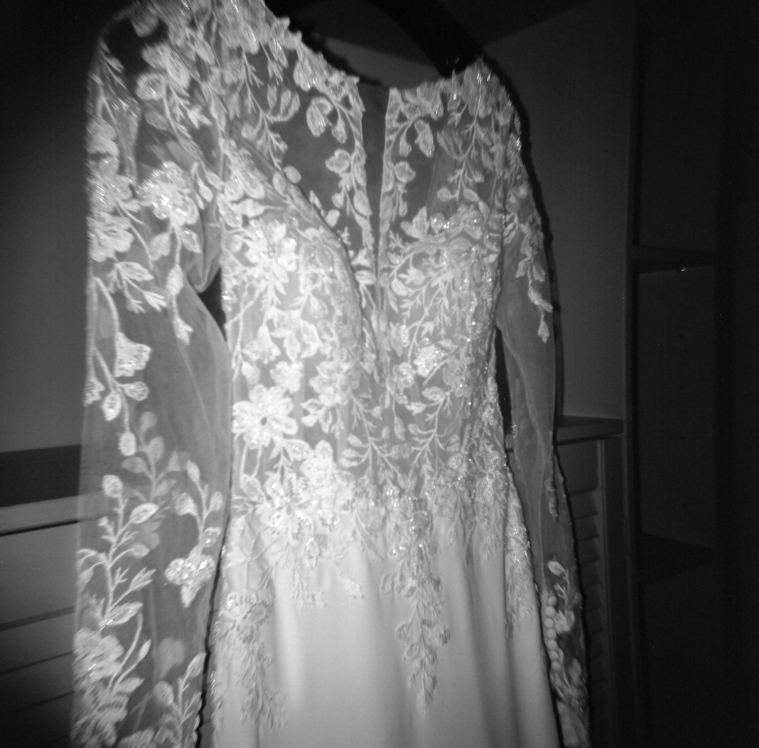 Close-up view of delicate lace and floral details on a white wedding dress hanging against a dark background.