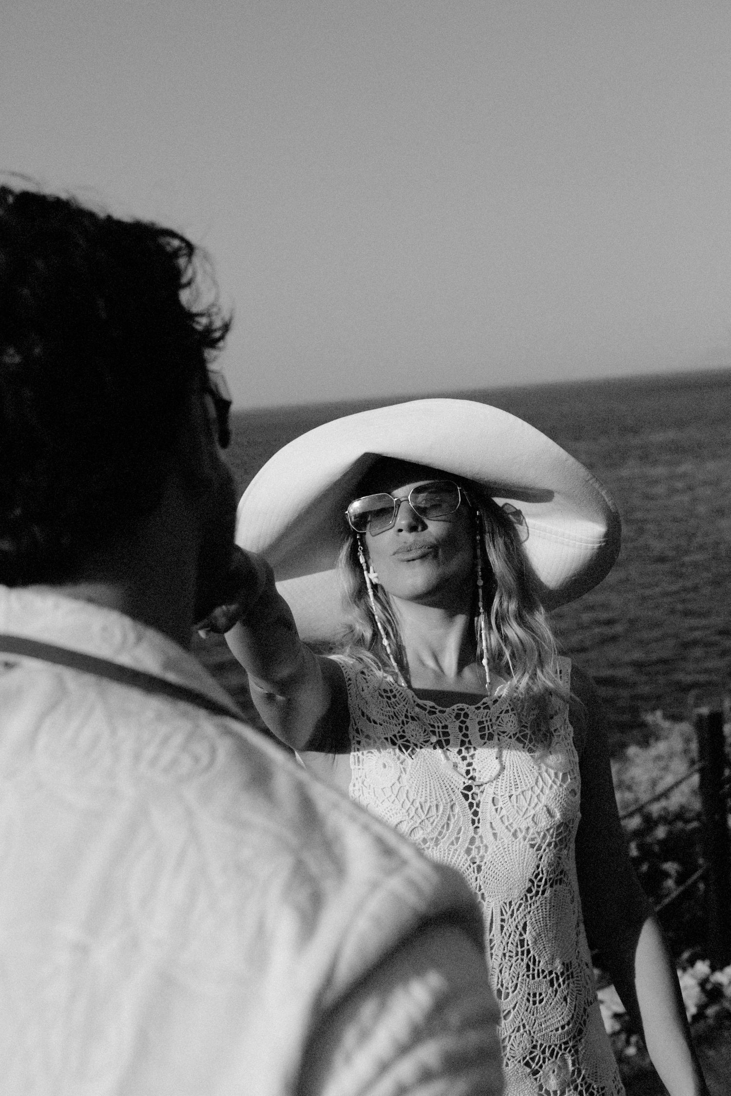 A romantic black and white photo series shows a couple in an intimate moment by the ocean, with sunlight and a white hat.