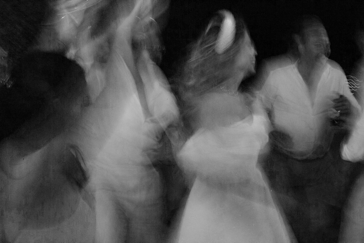 Blurry black and white photo of people dancing, capturing motion blur and ghostly movement at a social event.