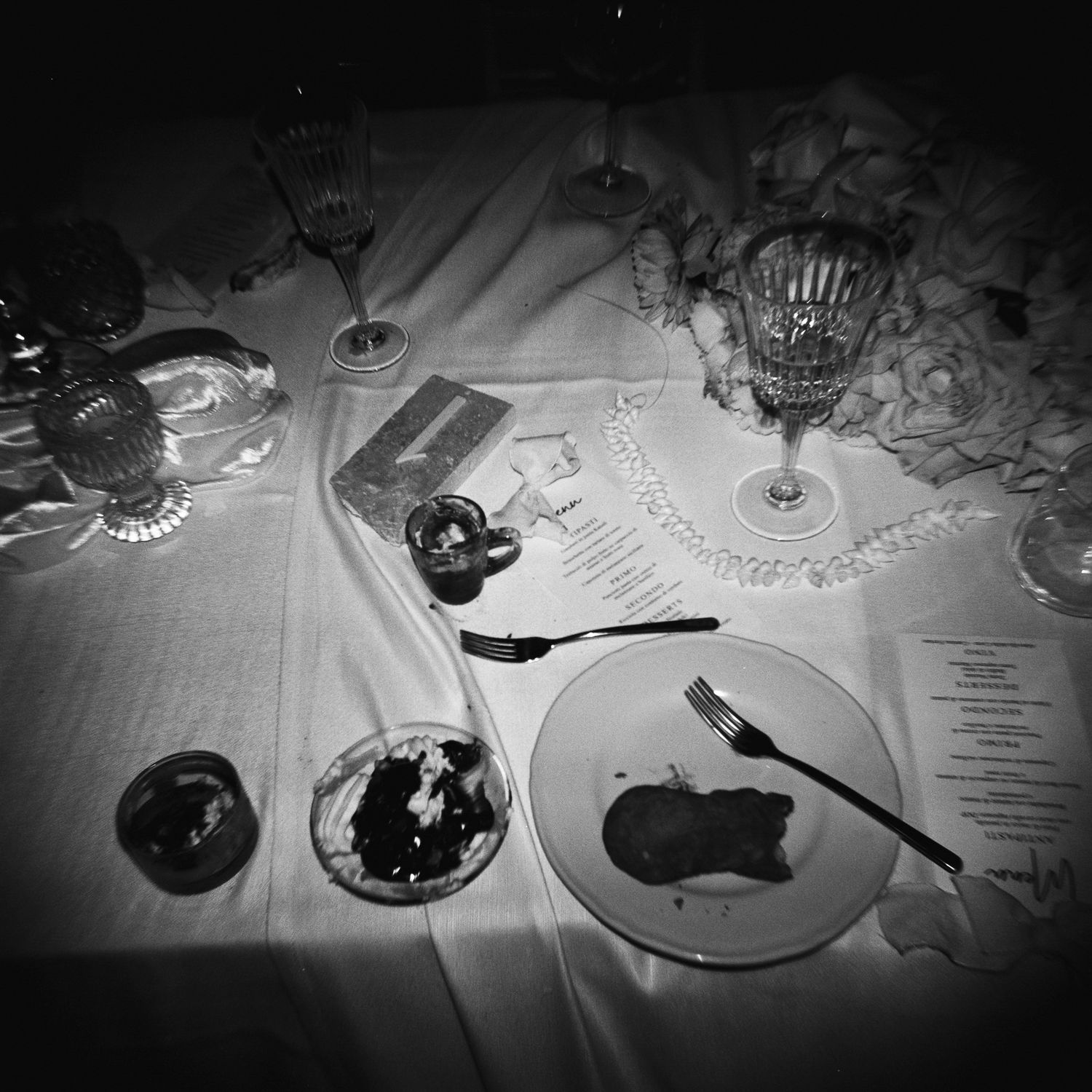 A series of black and white photographs showing plates of food and dining settings arranged in a dark, moody style.