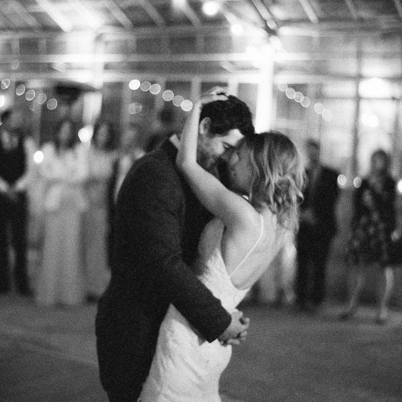 A couple shares their first dance at a wedding reception with soft lights and guests in the background.