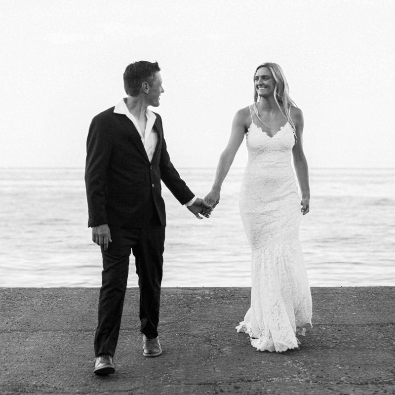 A black and white beach wedding photo series showing a couple walking together on the sand by the ocean.