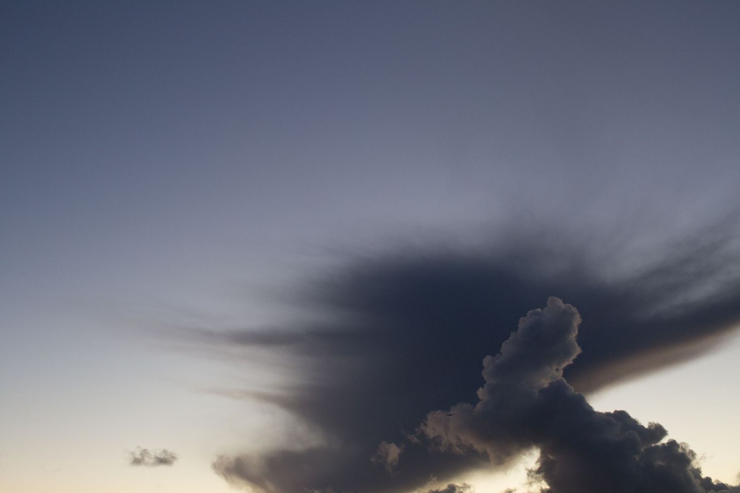 Dark storm clouds cast dramatic shadows against a dusky sky during sunset.