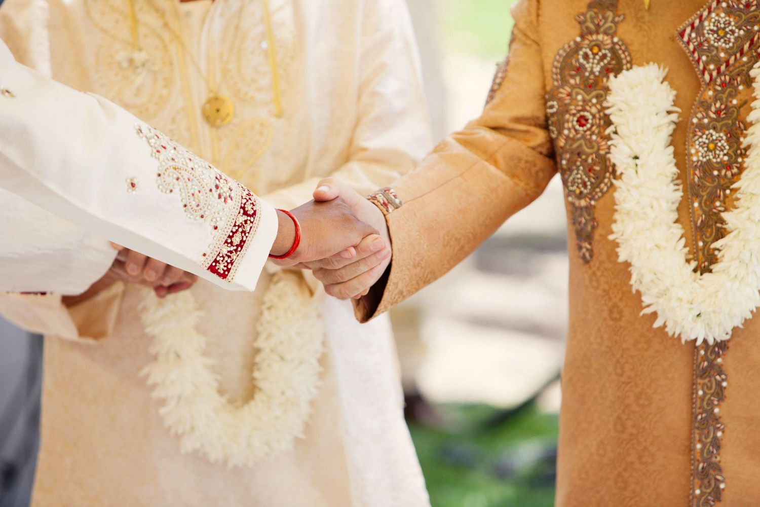 Close-up of hands during traditional Indian wedding ceremony with ornate outfits and garlands.
