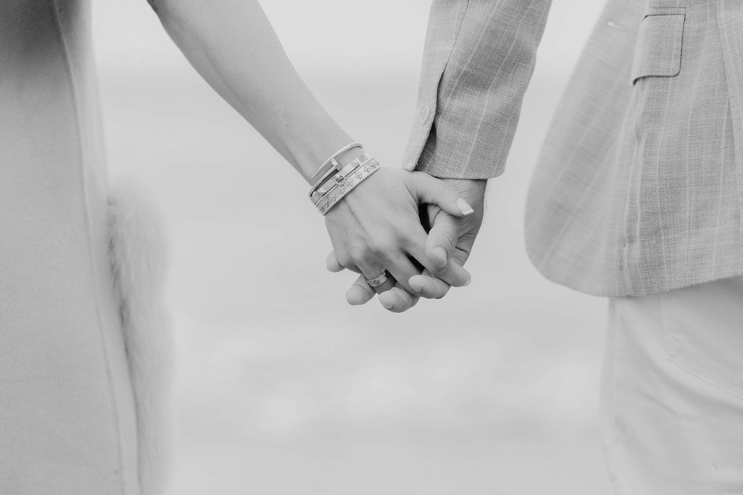 Black and white photo of a couple holding hands, woman wearing a bracelet, romantic outdoor setting.