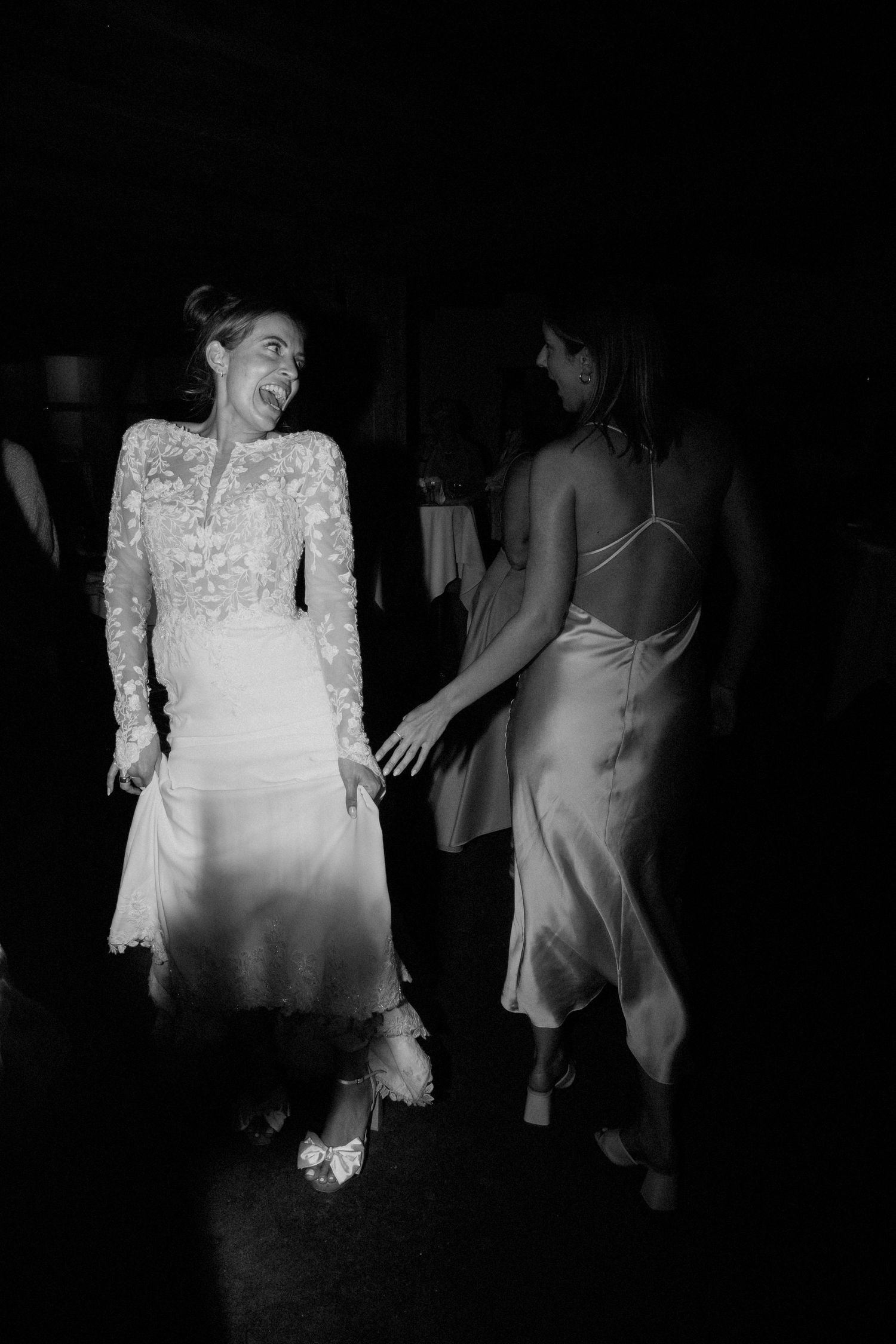 A black and white photo shows two people dancing at an event, one wearing a lace long-sleeved dress and another in a slip dress.