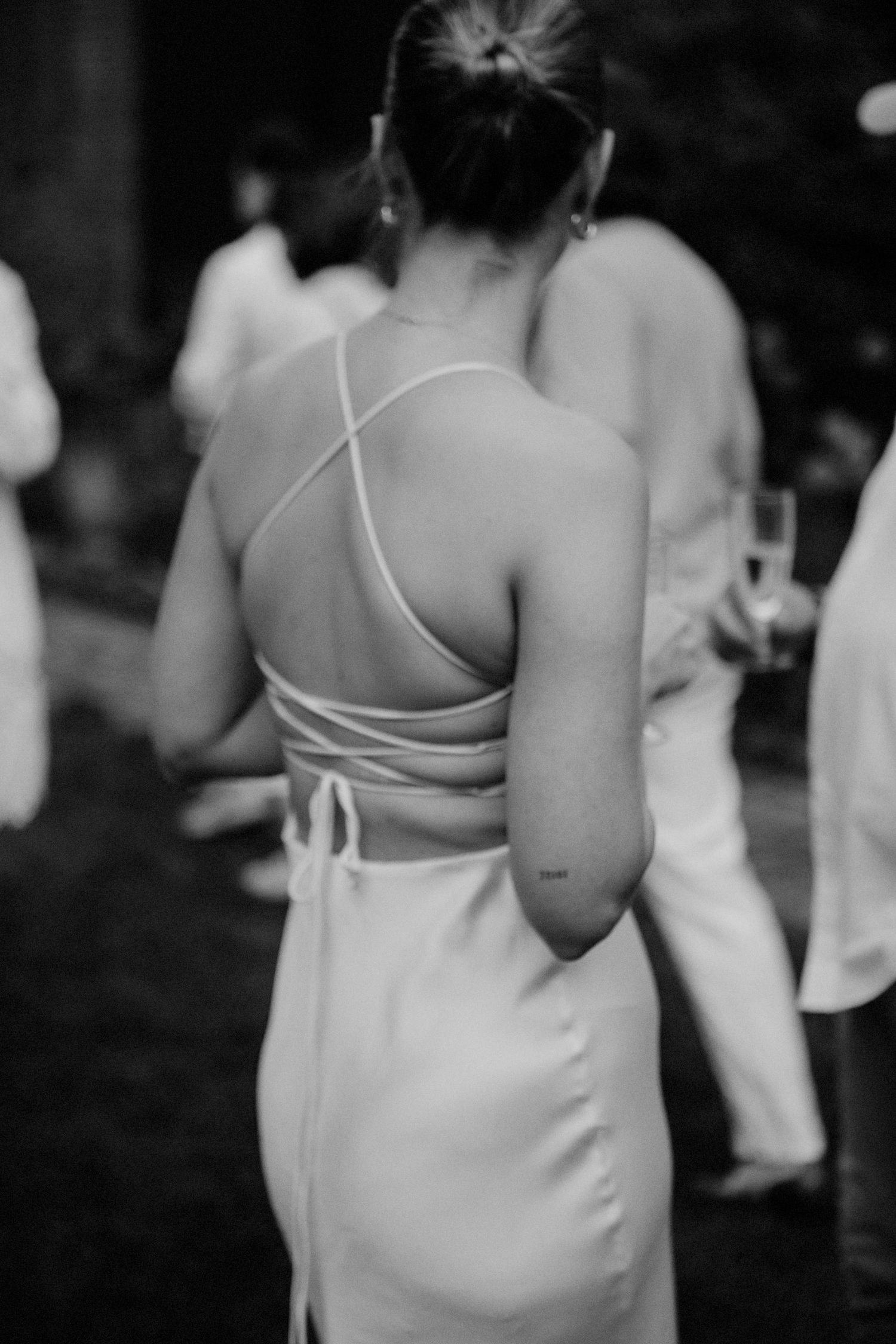Black and white photo of a woman in an elegant open-back halter dress at a formal outdoor event.