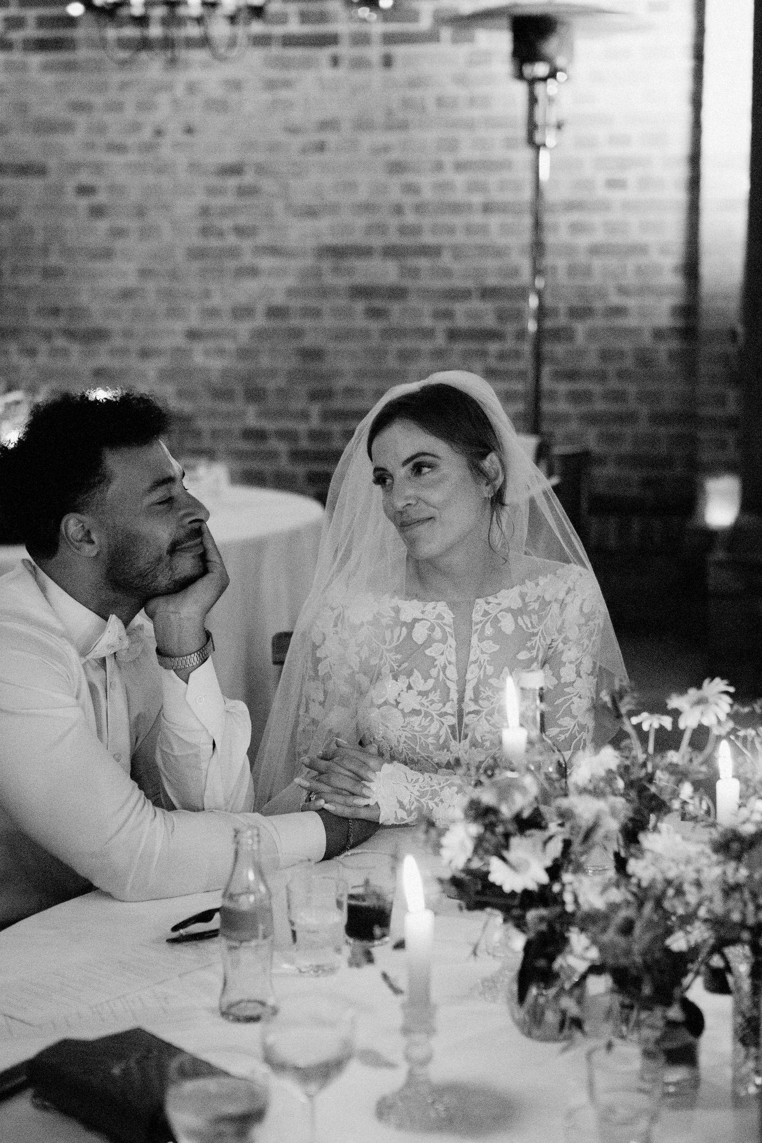 A romantic black and white wedding reception scene with a couple at a candlelit table with floral centerpieces.