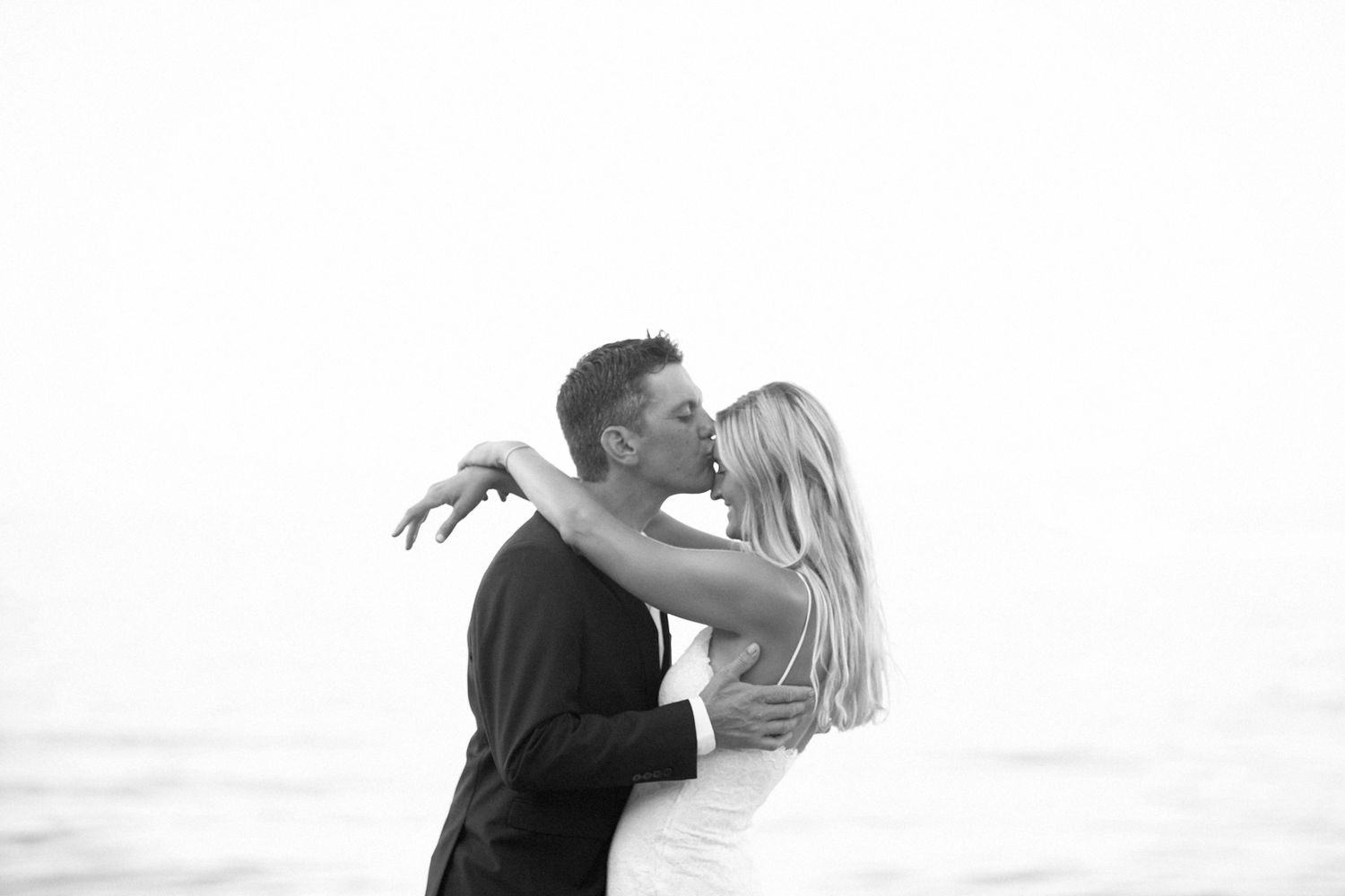 A romantic couple embraces on a beach at sunset in black and white silhouette.
