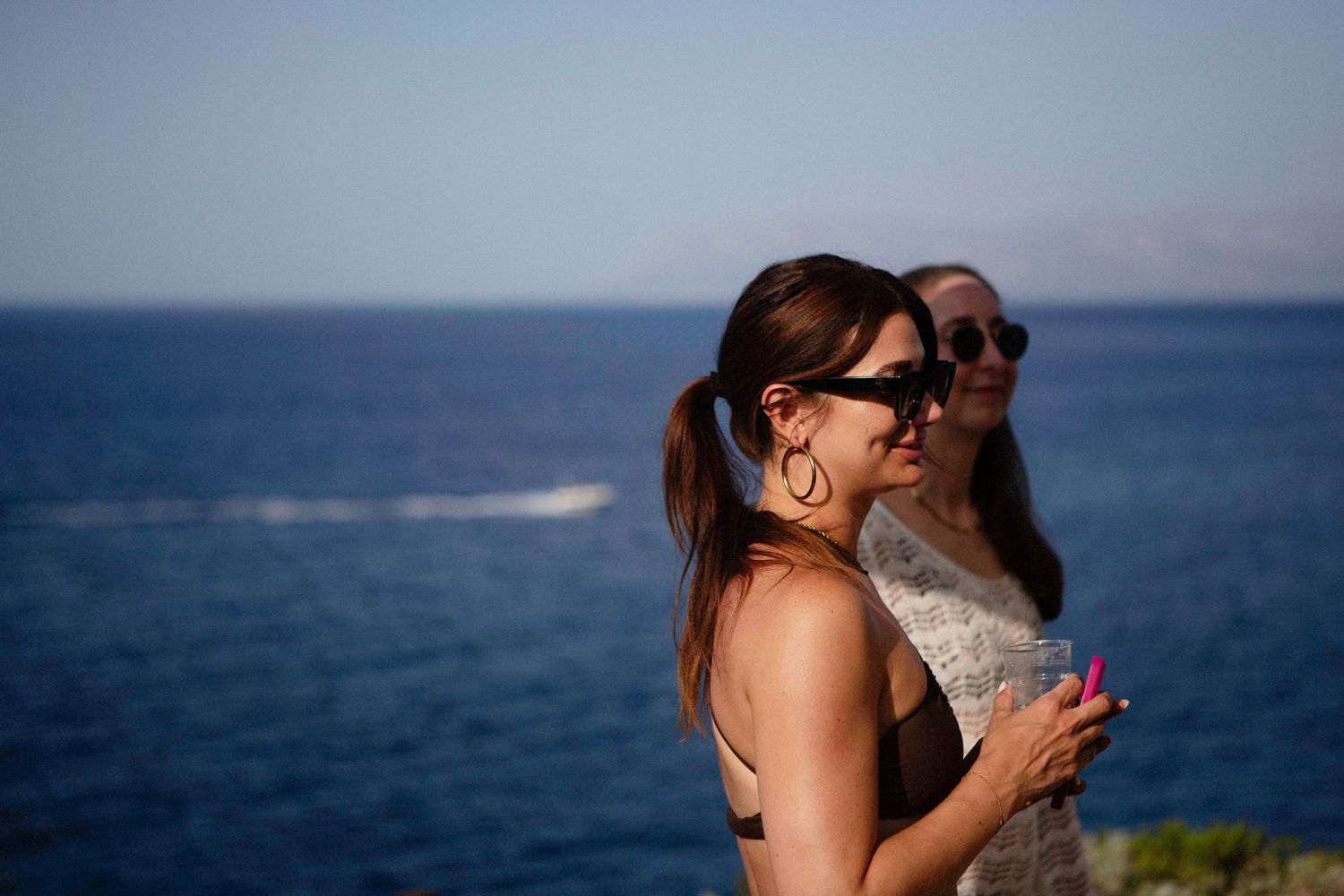 A couple embraces while standing on a coastal cliff overlooking the blue ocean on a sunny day.