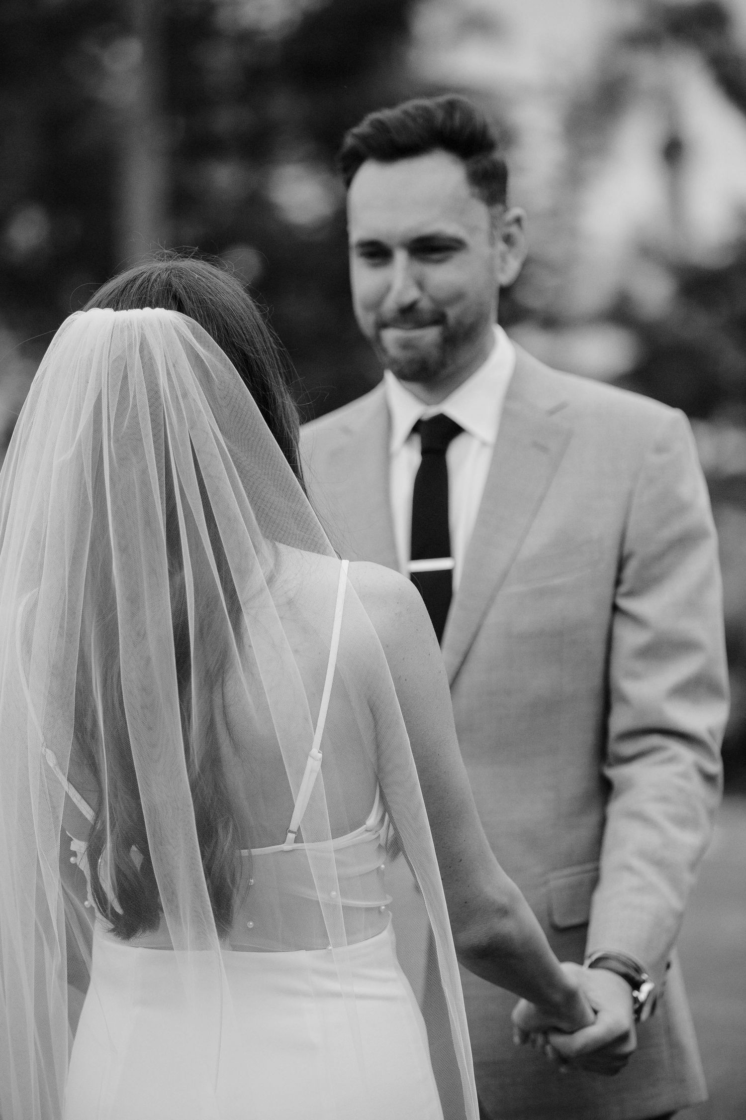 A series of black and white wedding photos showing the back of a bride in a veil with groomsmen in light colored suits.