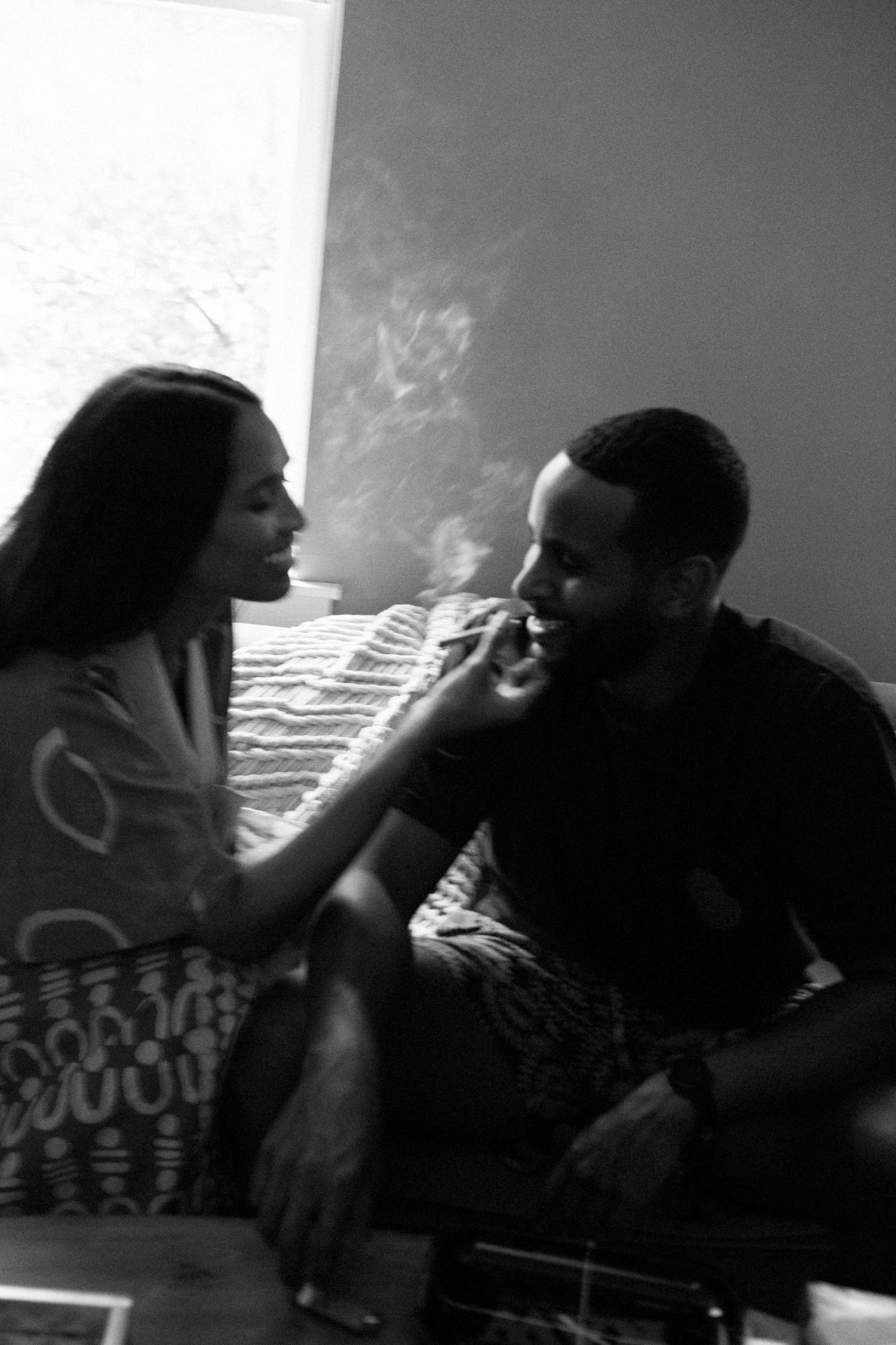 A black and white photograph shows a man and a woman sitting close together and interacting intimately.