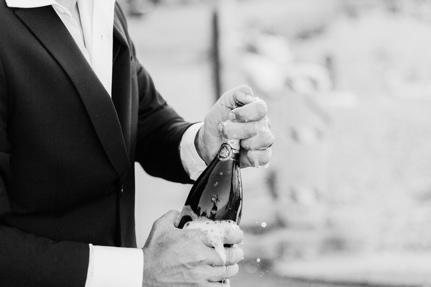 A person in formal attire opens a champagne bottle in black and white photography.