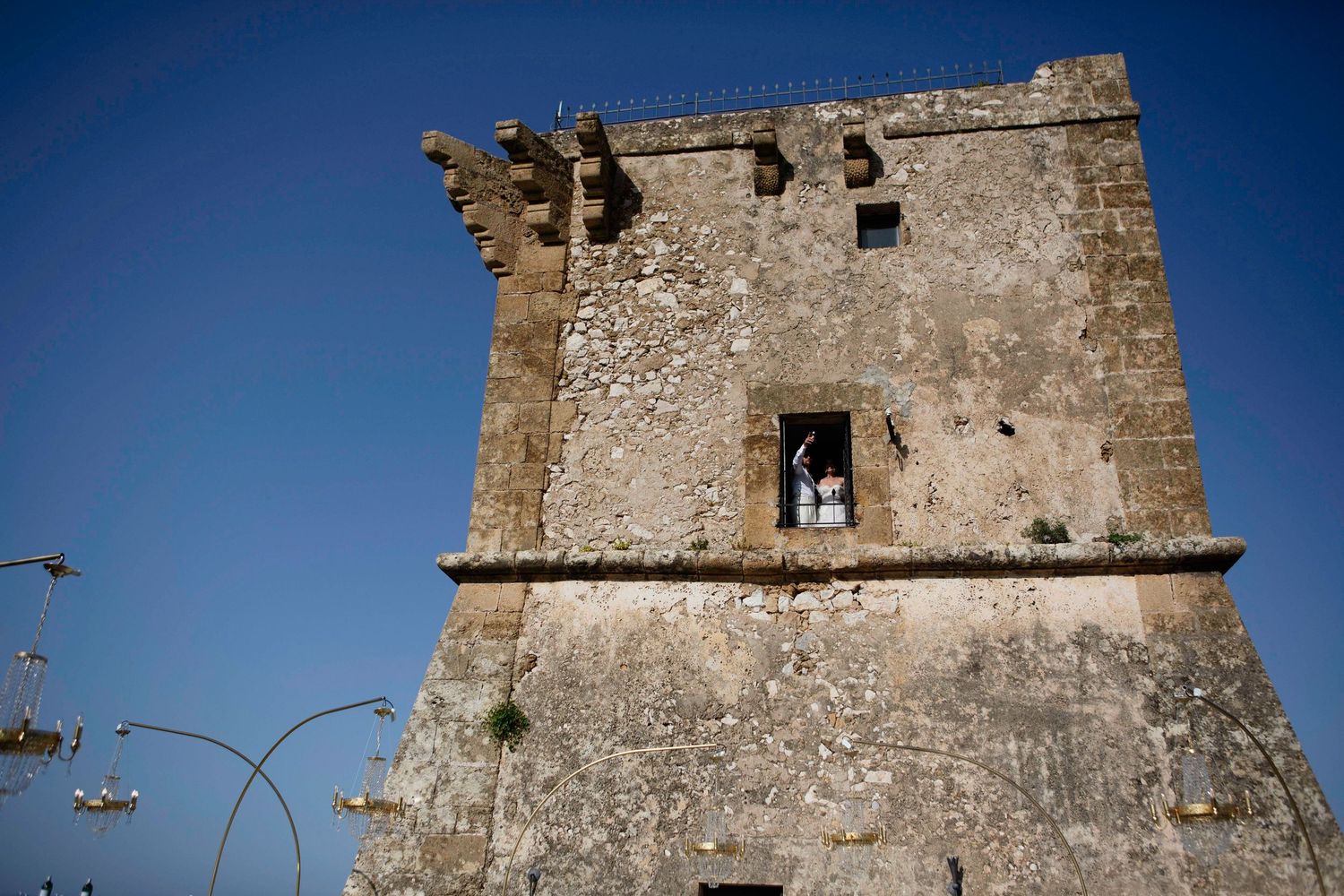 Ancient stone watchtower stands against deep blue sky with a helicopter flying past in Mediterranean coastal setting.
