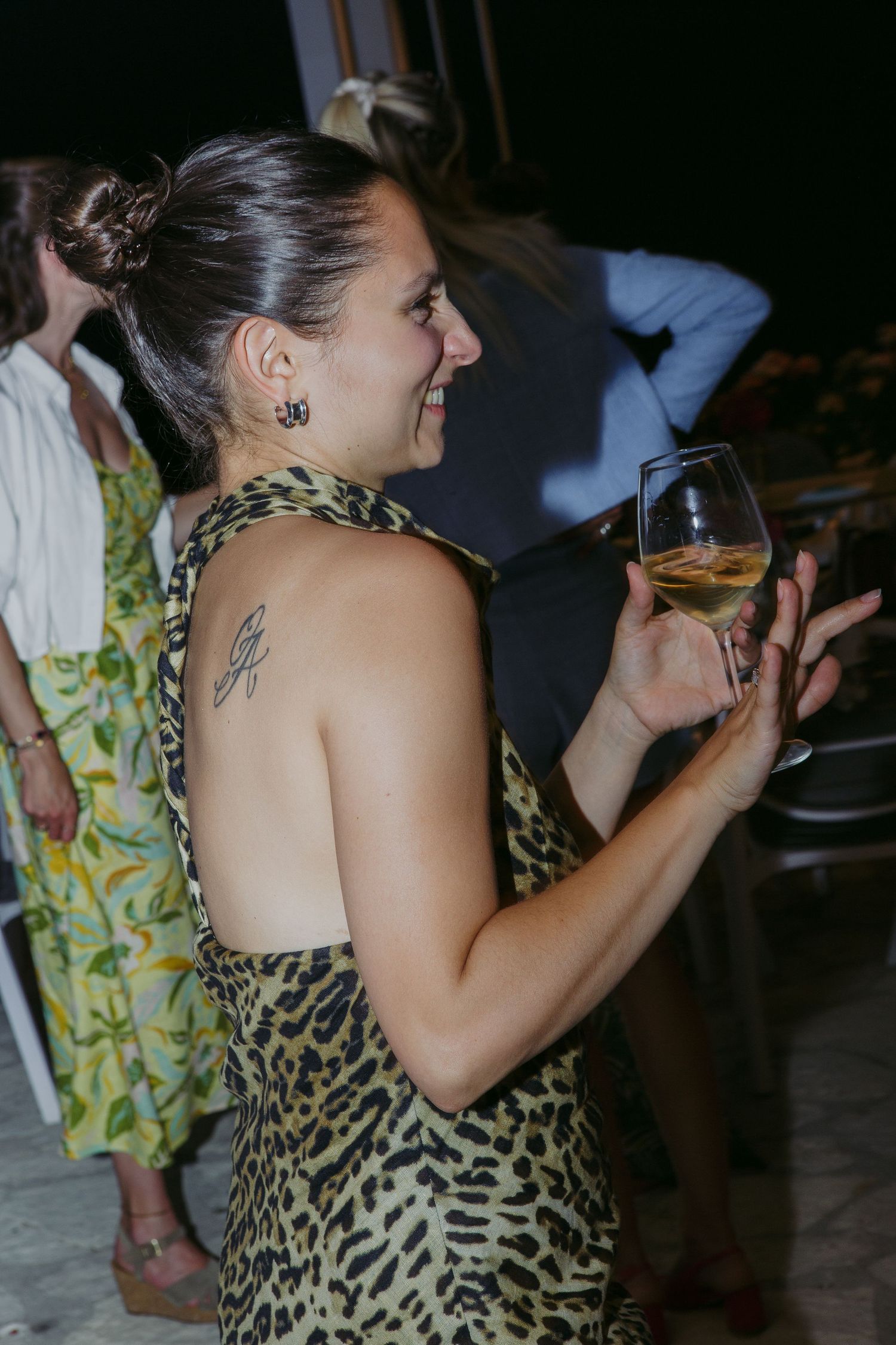 Person in leopard print dress holds wine glass while dancing at nighttime party.