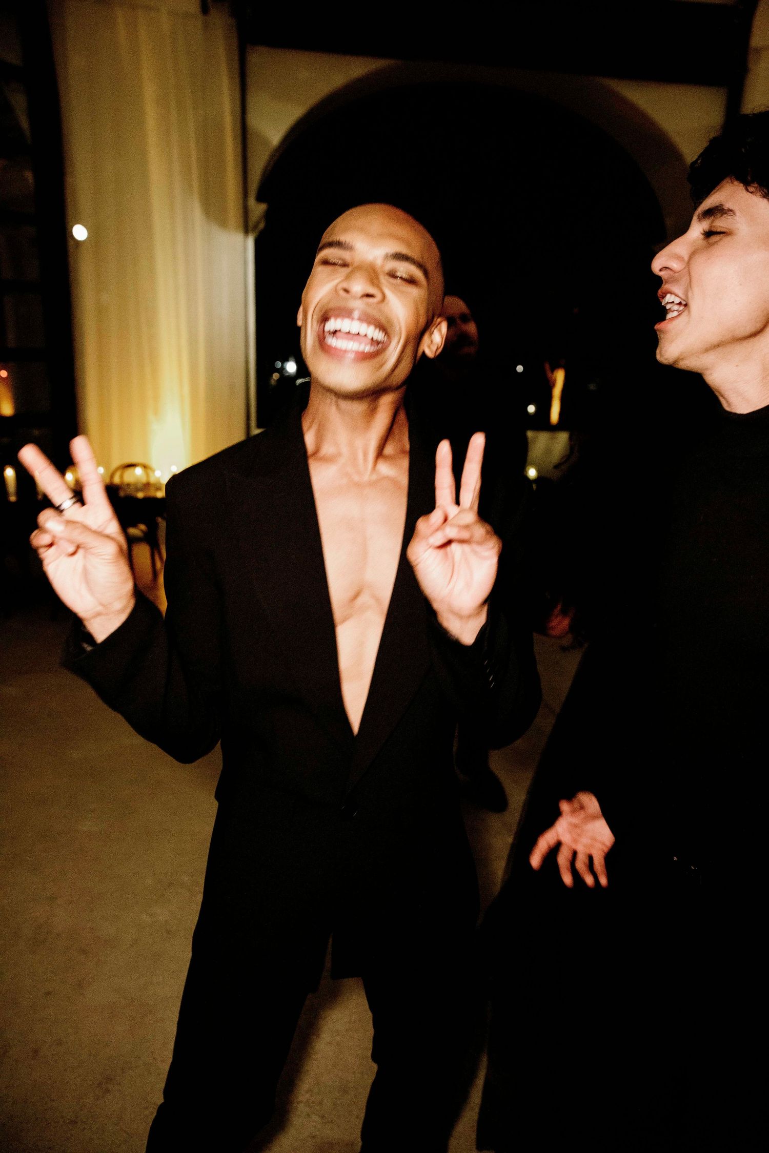 A series of candid photos showing someone in a black blazer making joyful expressions and peace signs against a dark background.