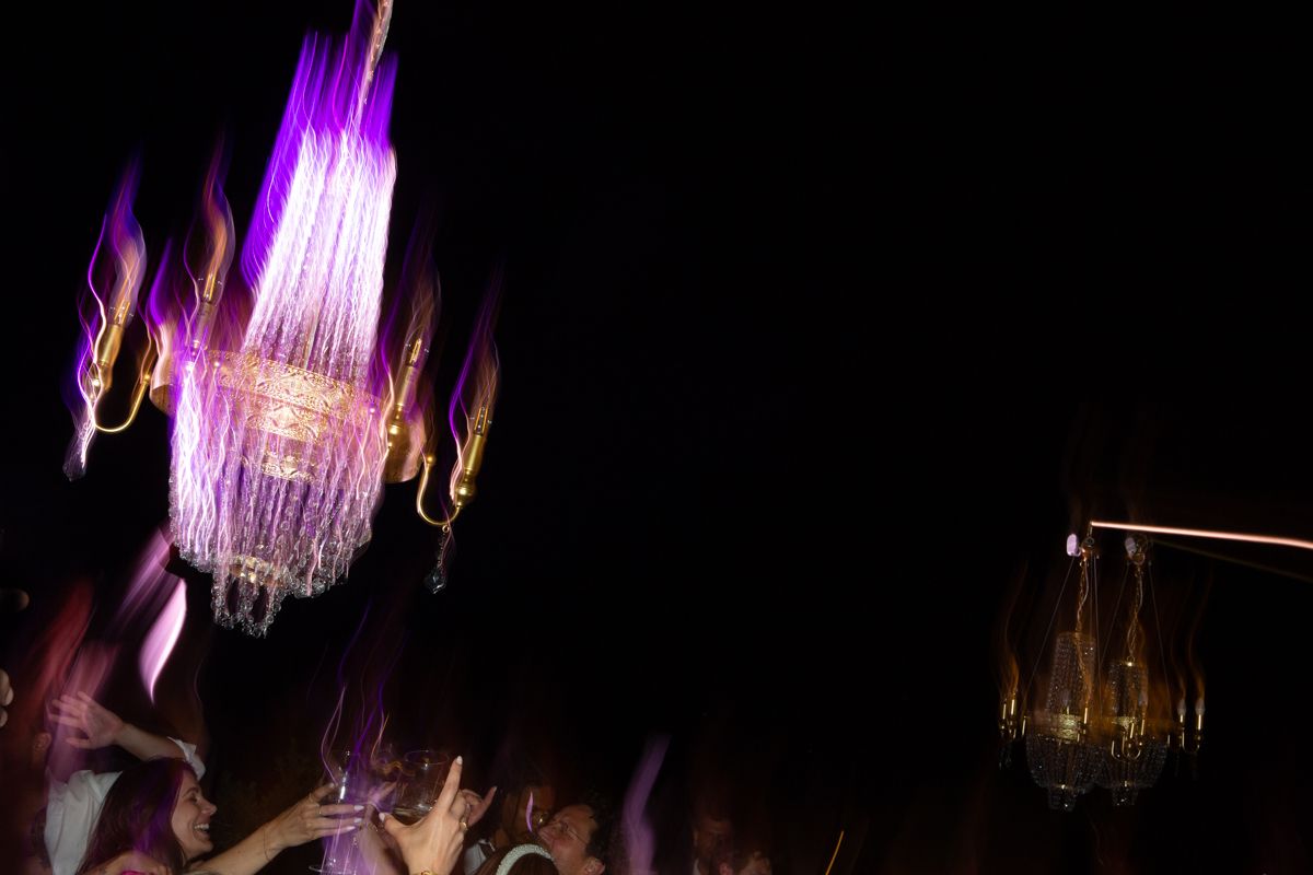 Illuminated crystal chandeliers glowing with purple and pink lights create an elegant atmosphere in a dark room.