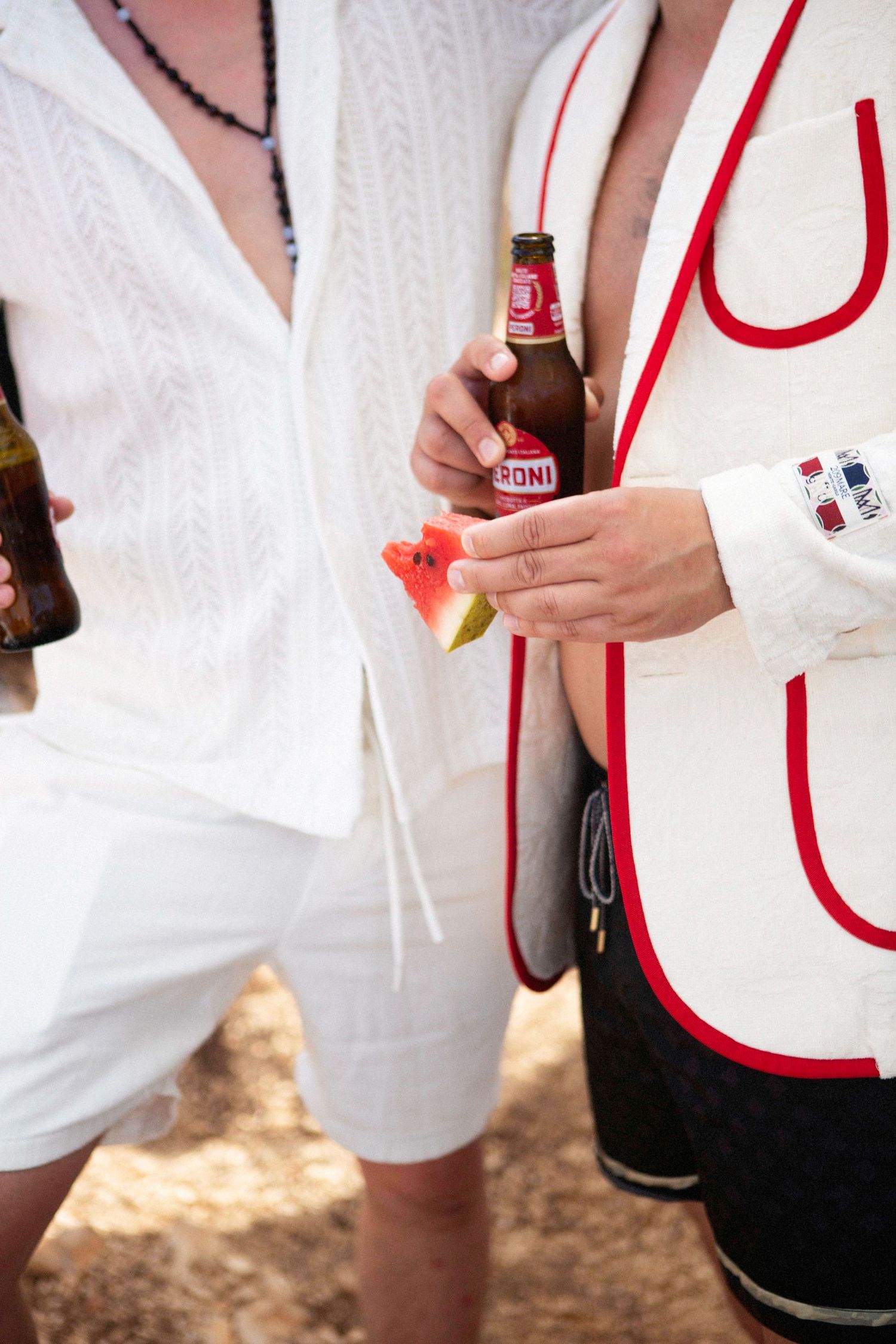 A person in white clothing holds a beverage bottle while standing outdoors.