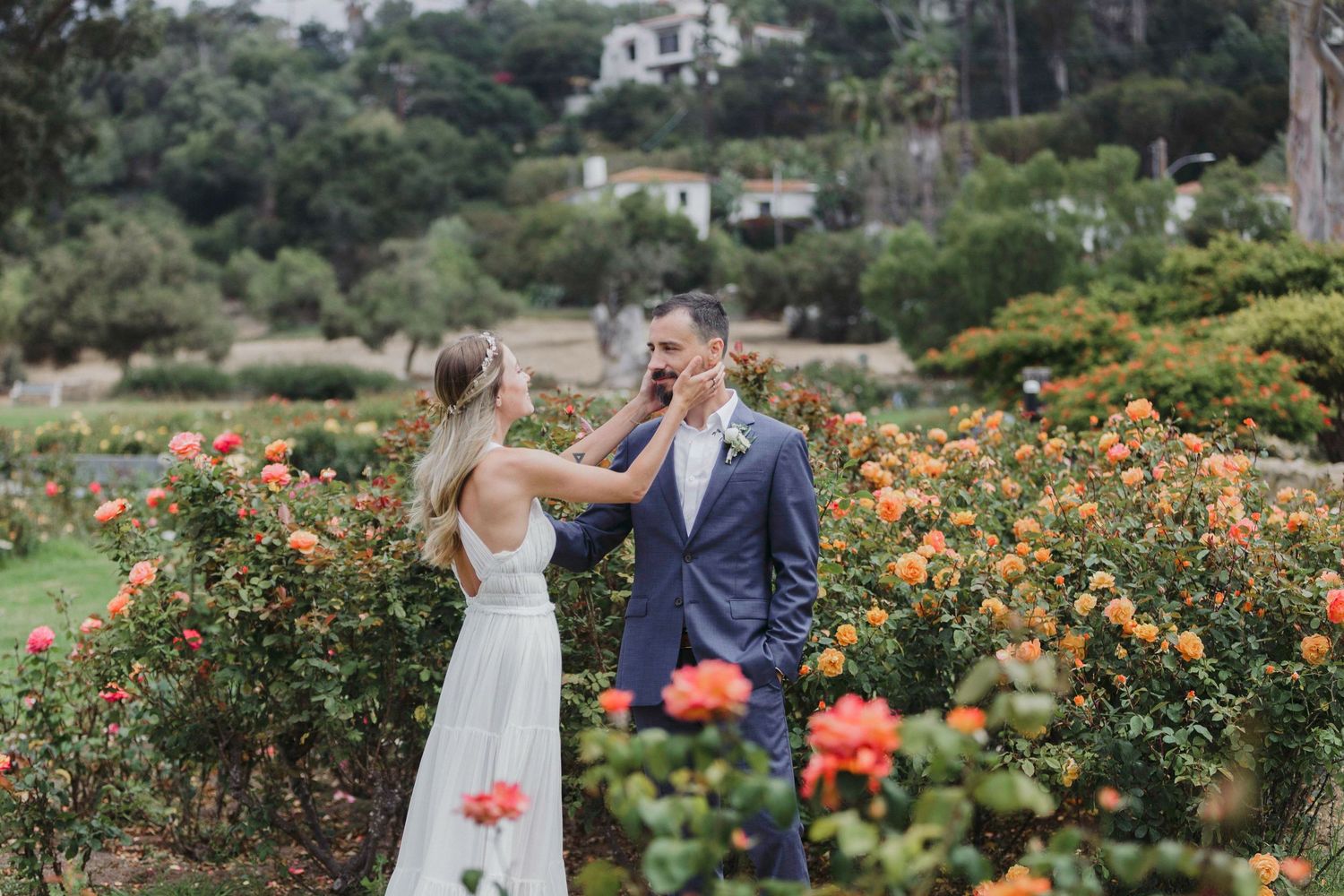 A couple shares a romantic moment in a lush garden filled with vibrant orange roses and greenery.