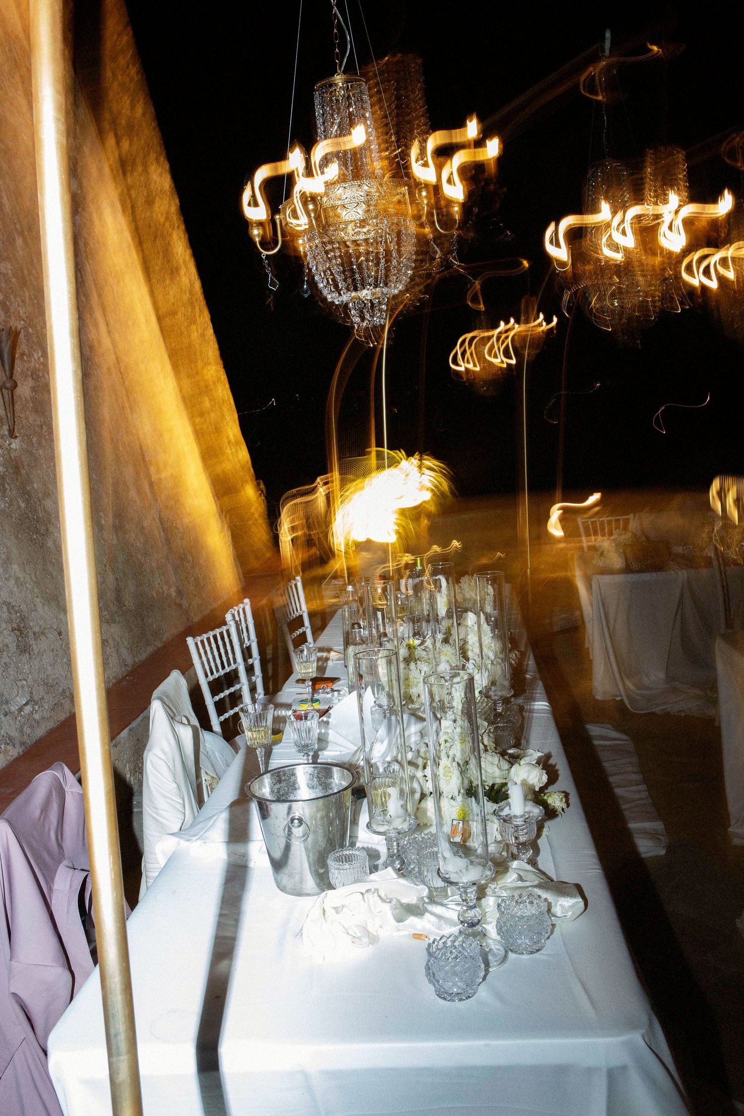 Elegant wedding reception tables with crystal chandeliers and white linens set for a formal dining event.