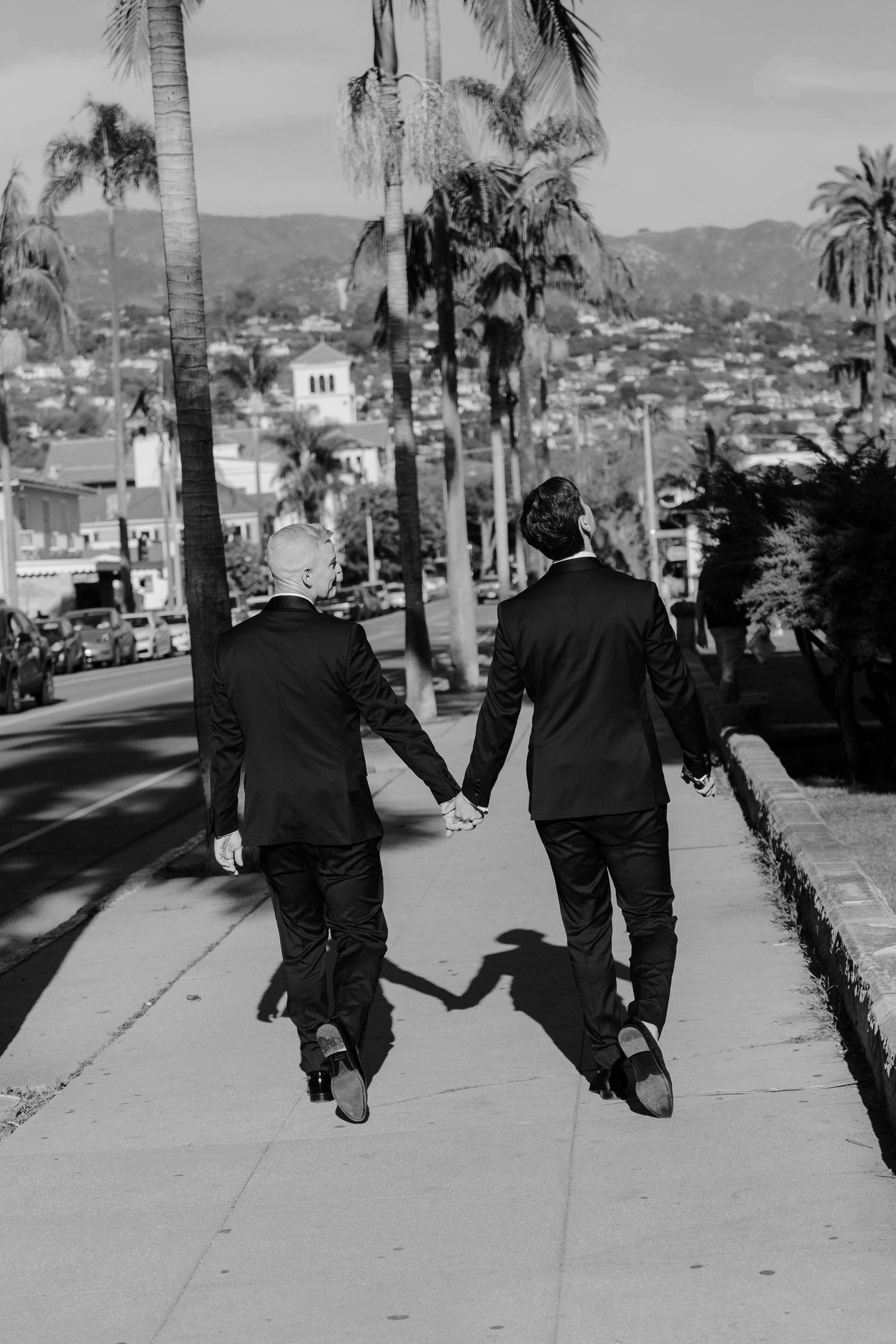 Black and white photo series of two people walking down a palm tree lined street in formal attire.