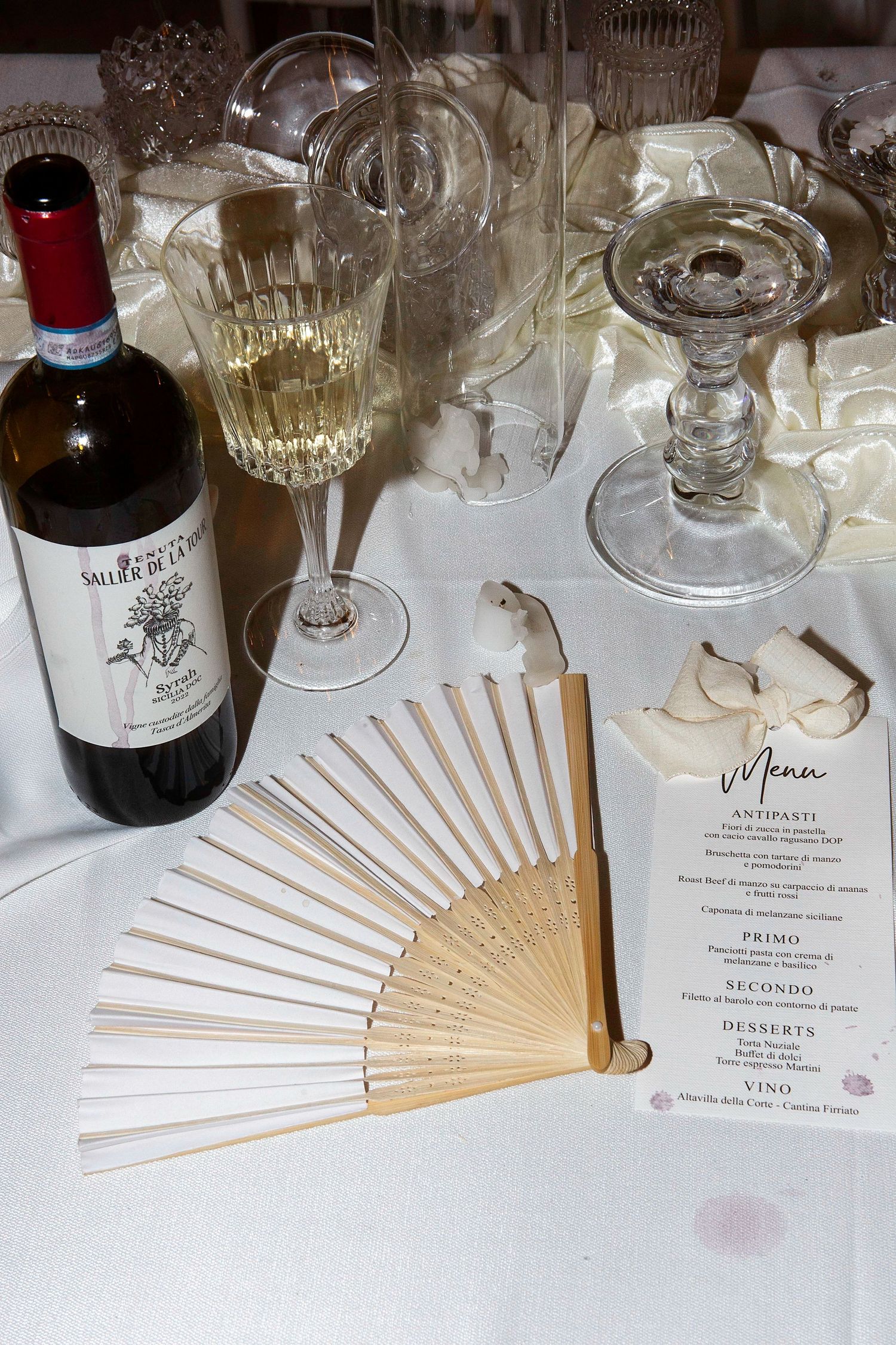 Elegant table setting with wine glasses, paper fans, and menu cards arranged for a formal dining event.