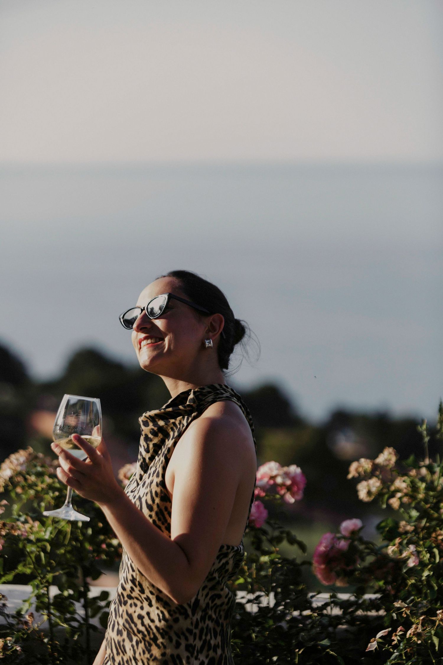 Someone in a leopard print dress enjoying wine at sunset in a vineyard or garden setting with flowers.