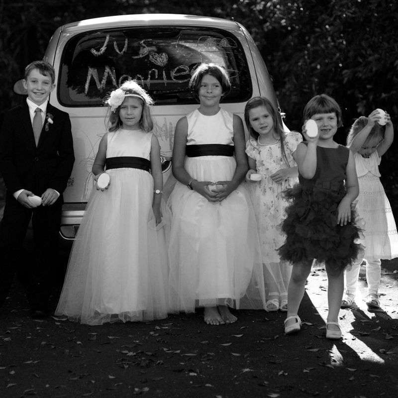 A group of children in white dresses and formal wear stand together outdoors in a black and white photograph.