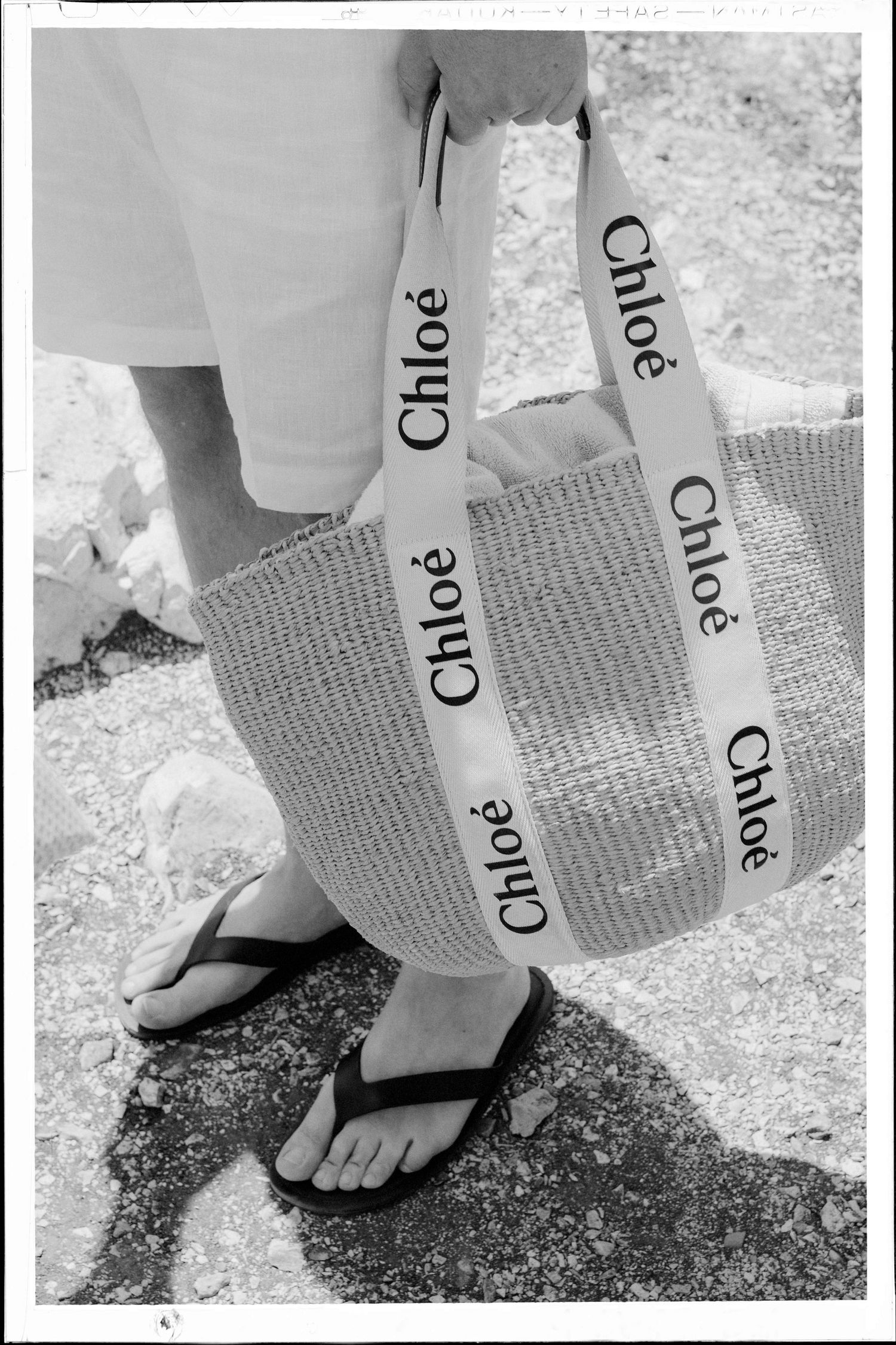 Close-up view of feet wearing white flip flops on textured ground with printed paper fragments visible.