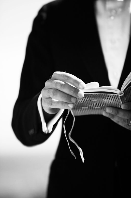 A black and white close-up of hands holding open books in a row, creating a repeating visual pattern.