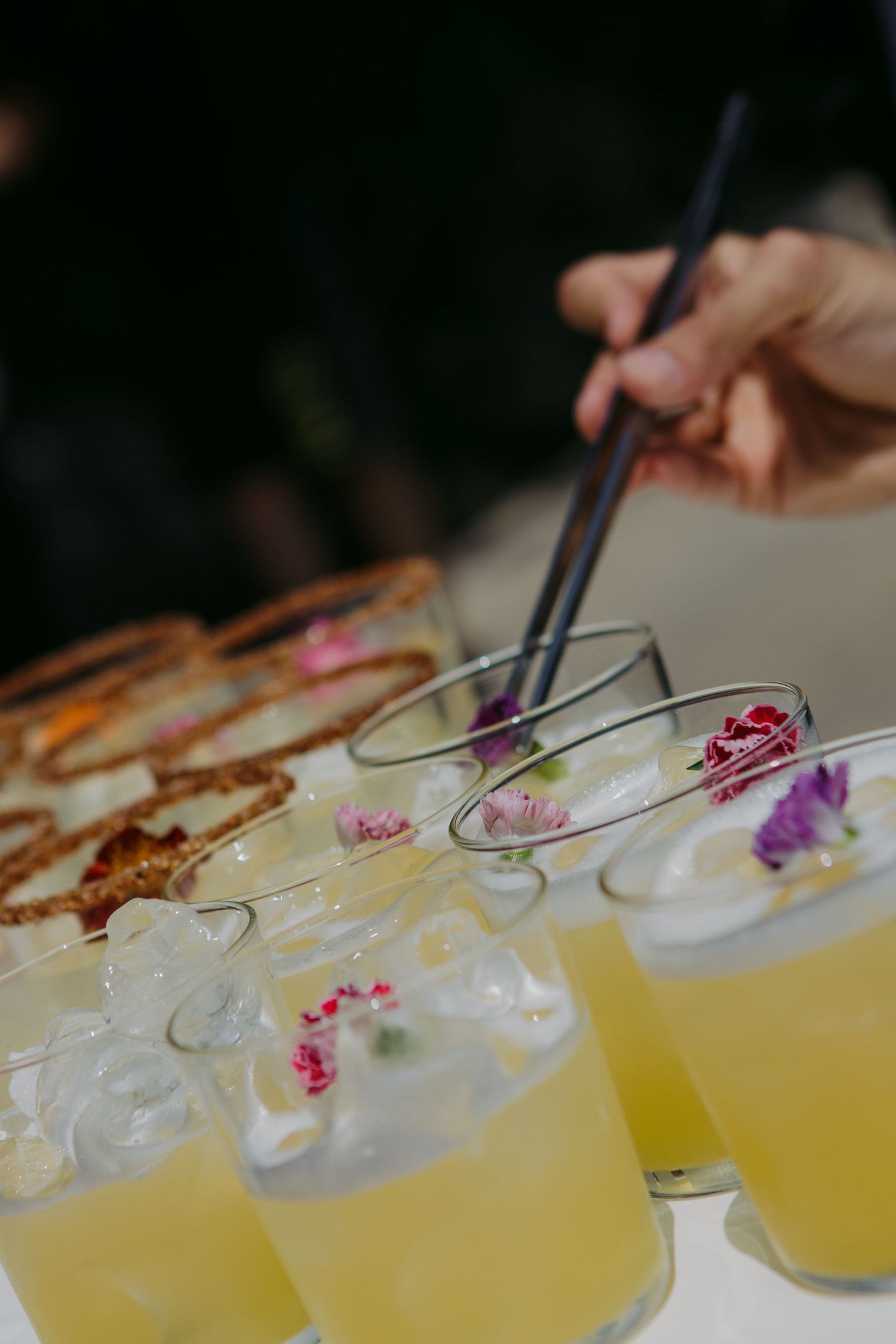 Yellow cocktails garnished with purple flowers and orange peels served in elegant martini glasses at a bar.